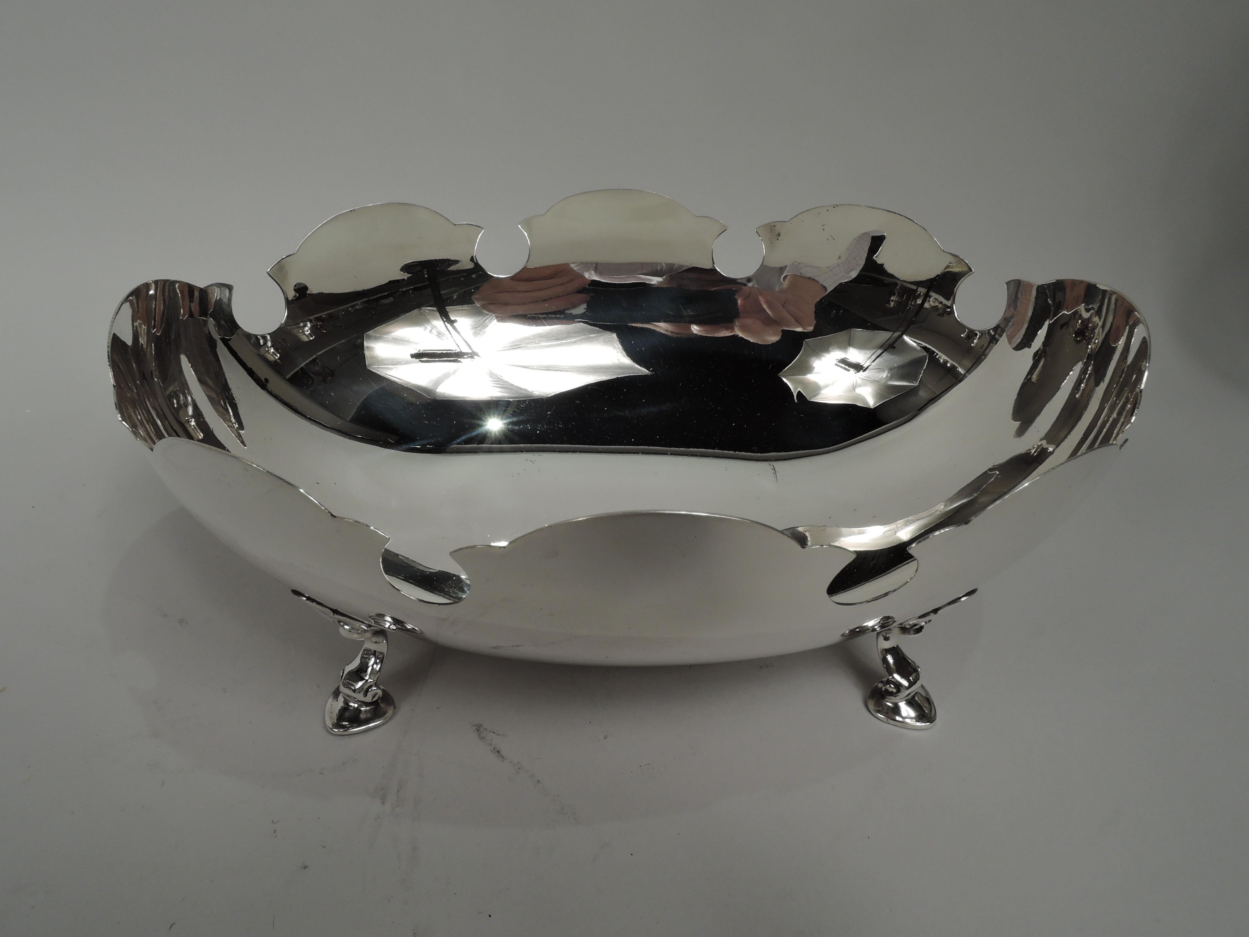 Mid-Century Modern sterling silver bowl. Made by Tiffany & Co. in New York. Ovoid with curved sides and 4 leaf-mounted volute-scroll hoof supports. Crisp and curved monteith-style rim with cutout circles. Fully marked including maker’s stamp and