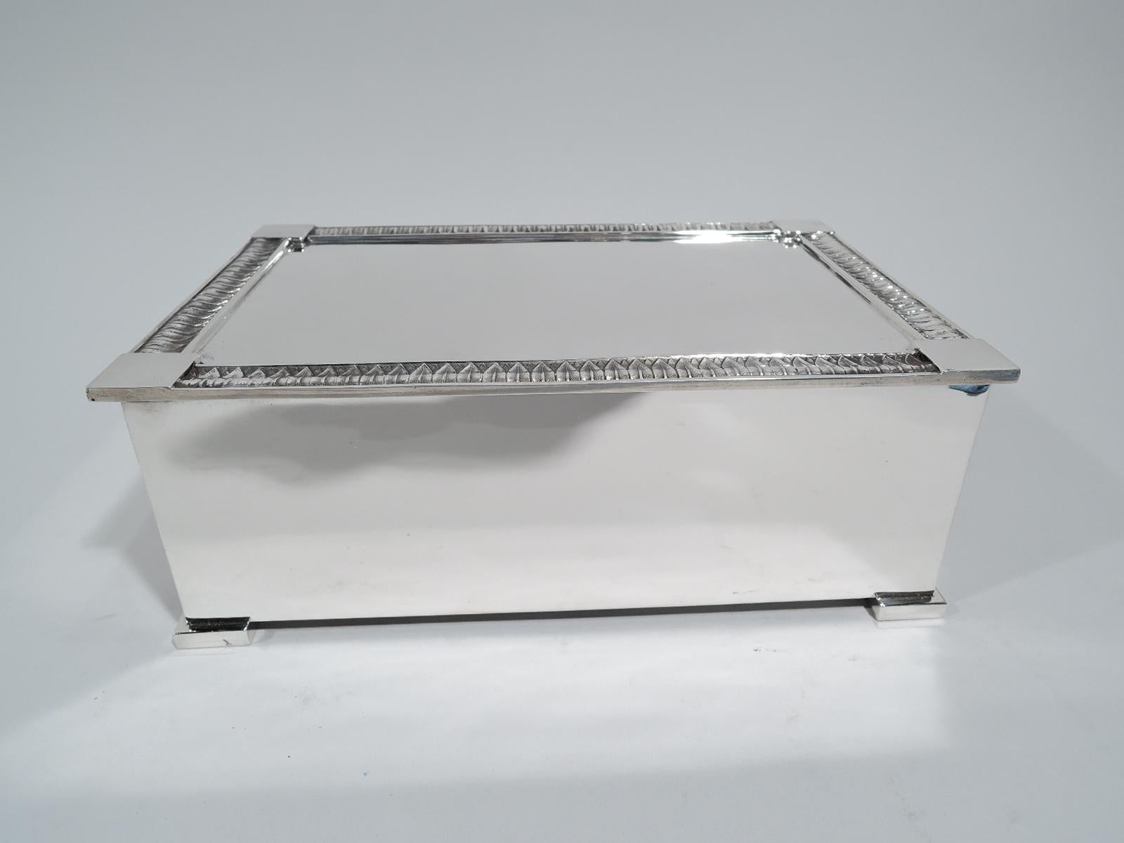 Modern classical sterling silver cigar box. Made by Tiffany & Co. in New York. Rectangular with straight sides and block supports. Cover flat, hinged, and overhanging with raised leaf-and-dart border and corner squares. Box interior cedar lined.