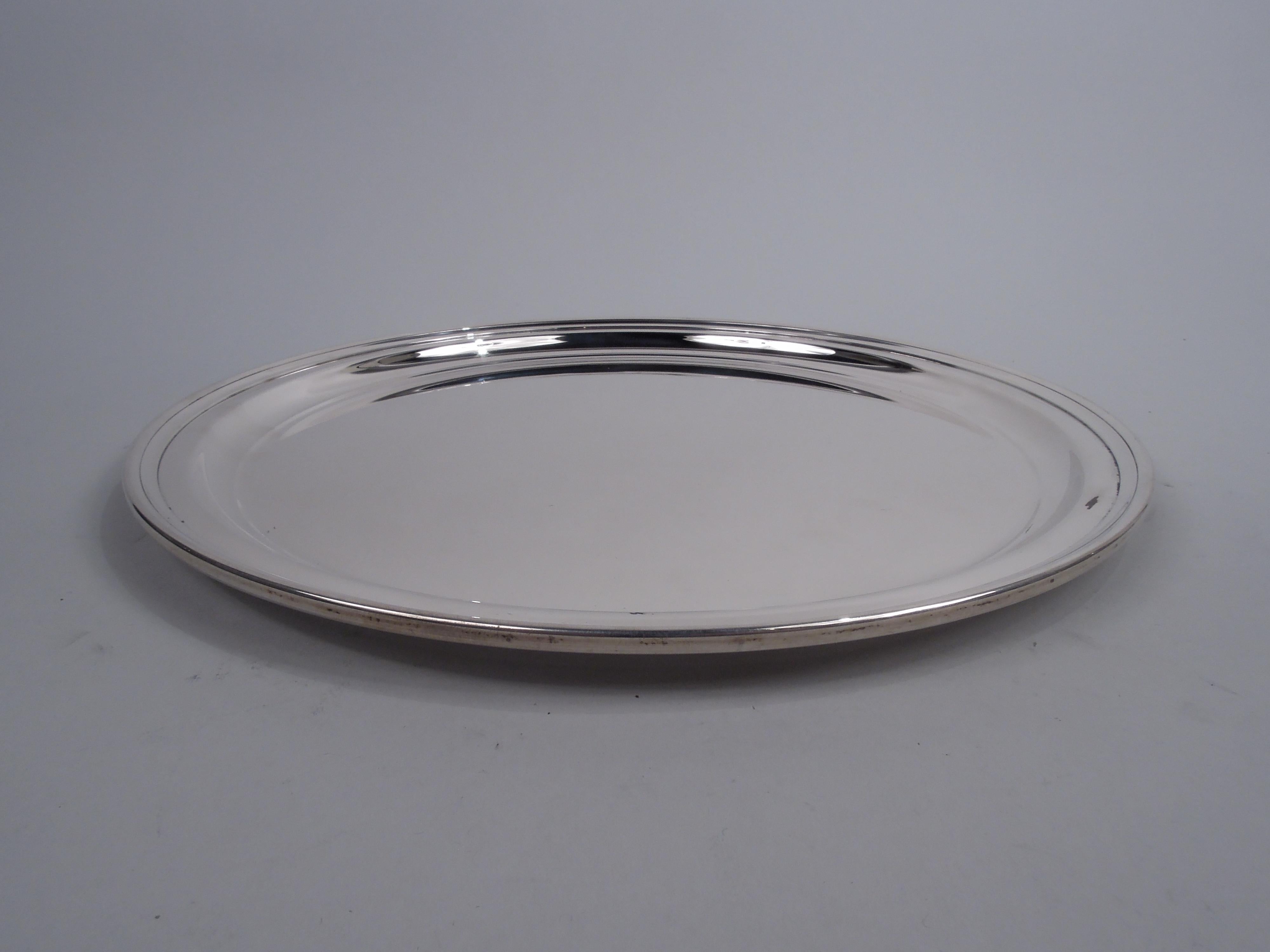 Classic Modern sterling silver serving tray. Made by Tiffany & Co. in New York, ca 1960. Round well, narrow shoulder, and plain rim with incised band. Heavy and well balanced. Fully marked including maker’s stamp and pattern no. 21153. Weight: 27