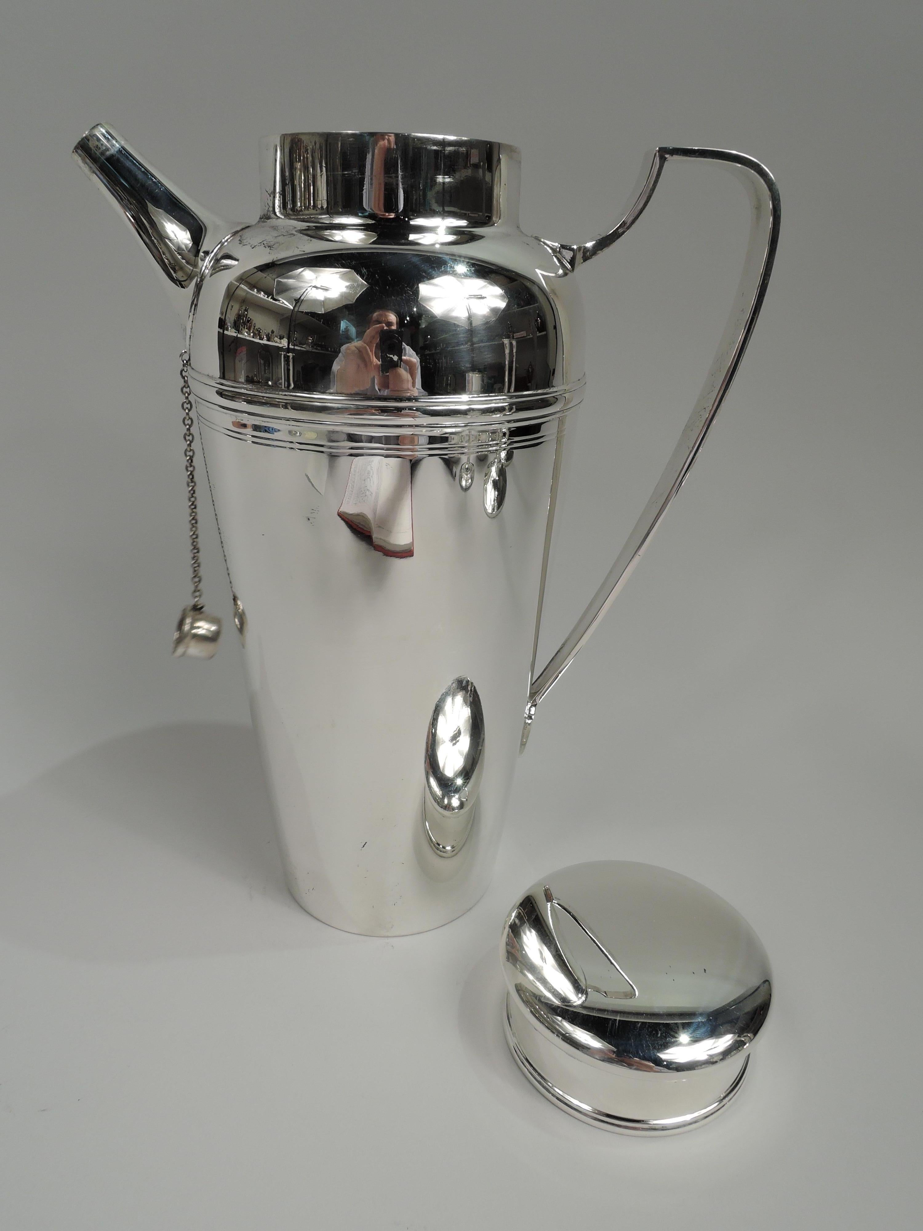 Party-size sterling silver cocktail shaker. Made by Tiffany & Co. in New York, ca 1929. Tapering bowl, curved shoulder, scrolled-bracket handle, stubby tapering spout with built-in strainer and chained cap, and short neck with flat, over hanging
