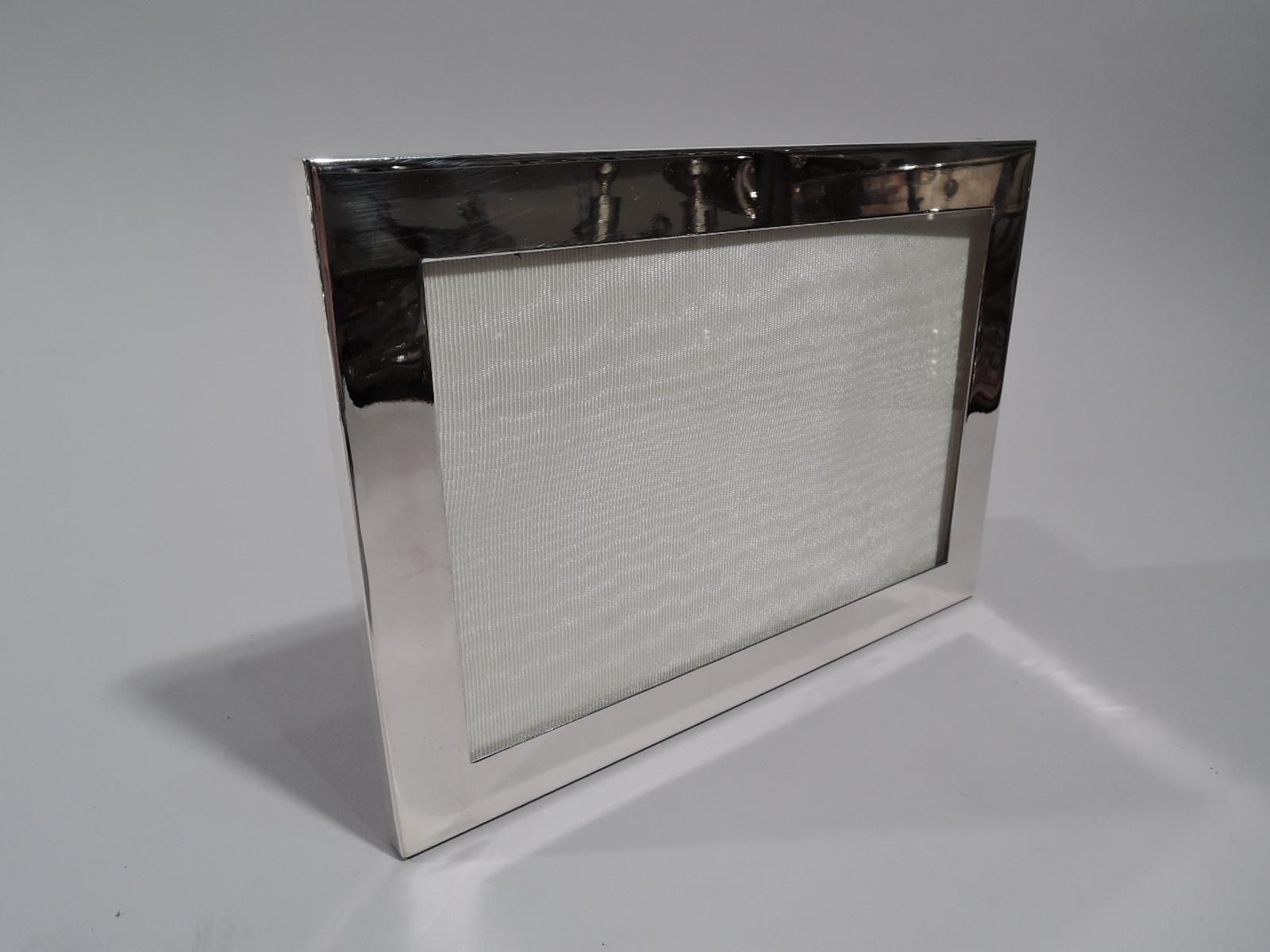 Modern sterling silver picture frame. Retailed by Tiffany & Co. in New York. Rectangular window in flat surround with glass, silk lining, and velvet back and hinged support. For portrait (vertical) or landscape (horizontal) display. Marked “Tiffany
