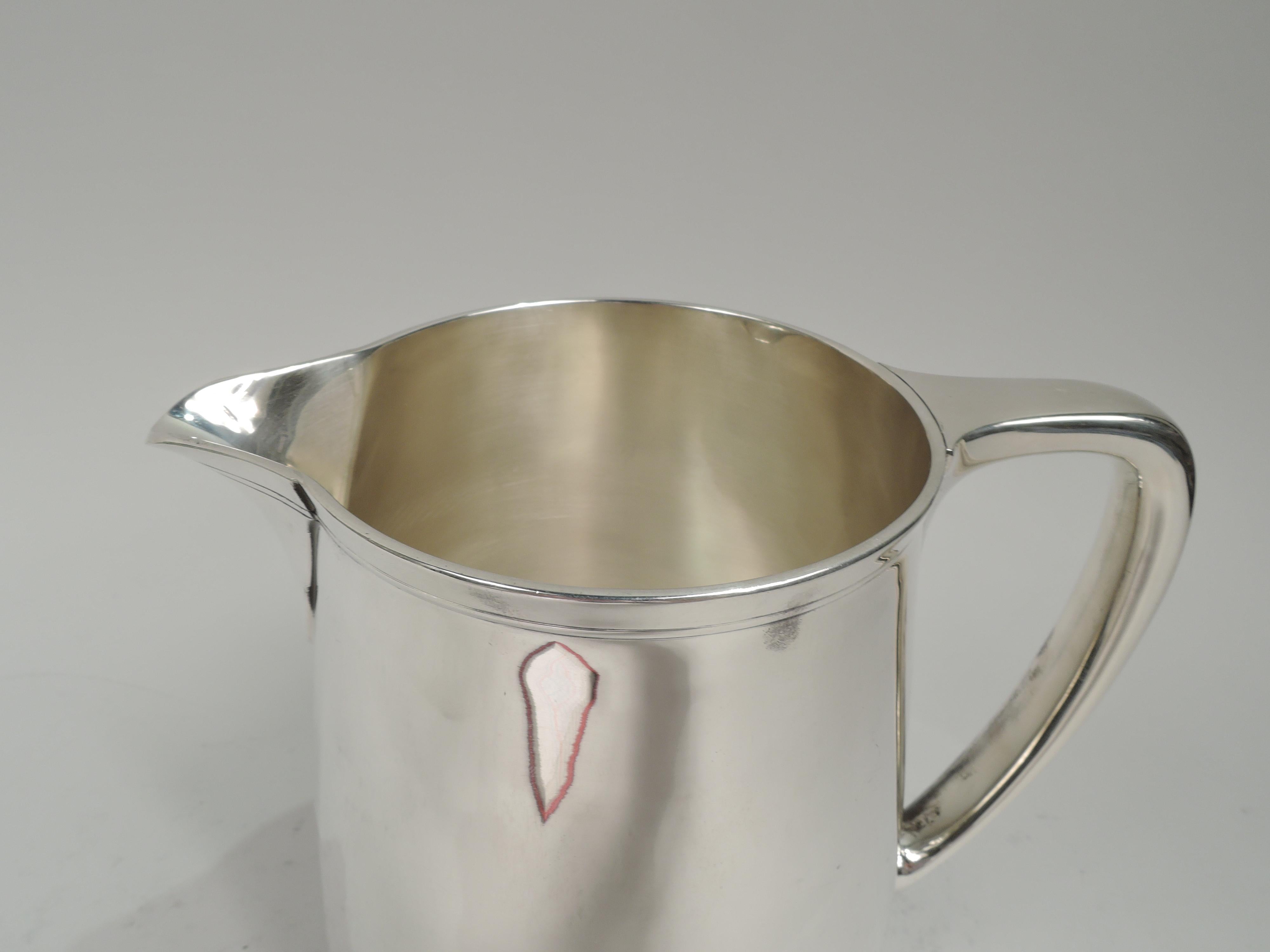 Modern sterling silver water pitcher. Made by Tiffany & Co. in New York, ca 1923. Upward tapering sides, scrolled bracket handle, and v-spout. Spare incised banding near rim. Fully marked including maker’s stamp, pattern no. 20210 (first produced in
