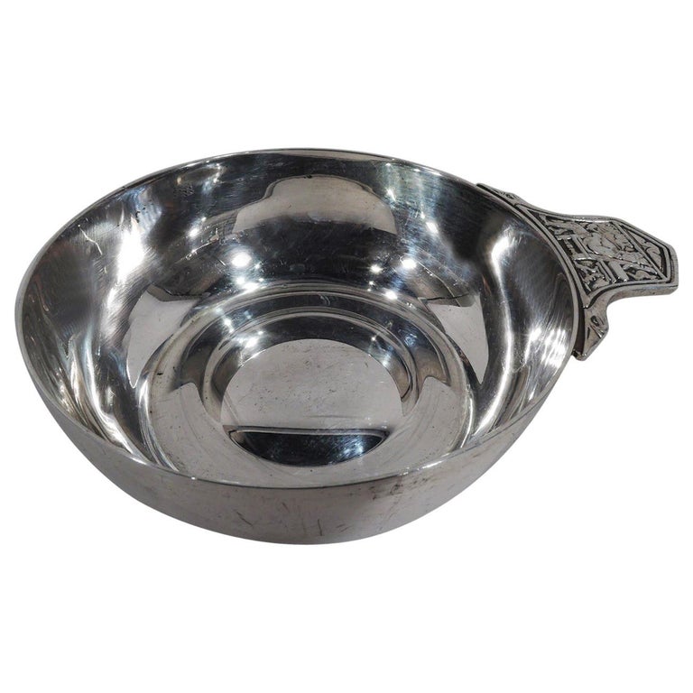 Nursery rhyme-themed sterling silver porringer. Made by Tiffany in New York. Round and curved. Handle solid and curvilinear with goose neck mounts. On handle is low-relief depiction of Old King Cole, who has 