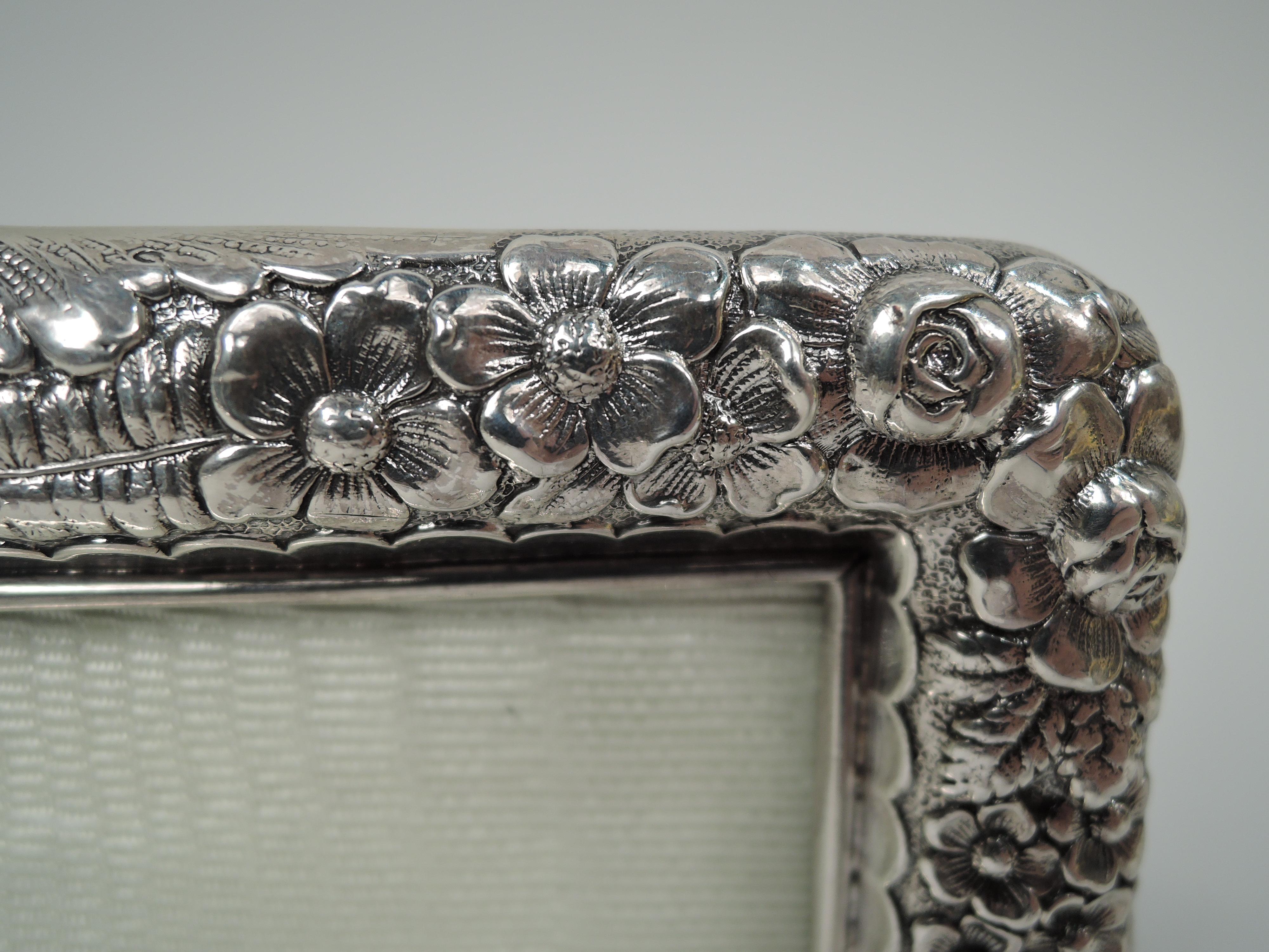Victorian sterling silver picture frame. Made by Tiffany & Co. in New York. Rectangular window in same surround with scalloped interior border, curved corners, raised leaf-wrapped top center, splayed same corner supports. Dense leaf and flower