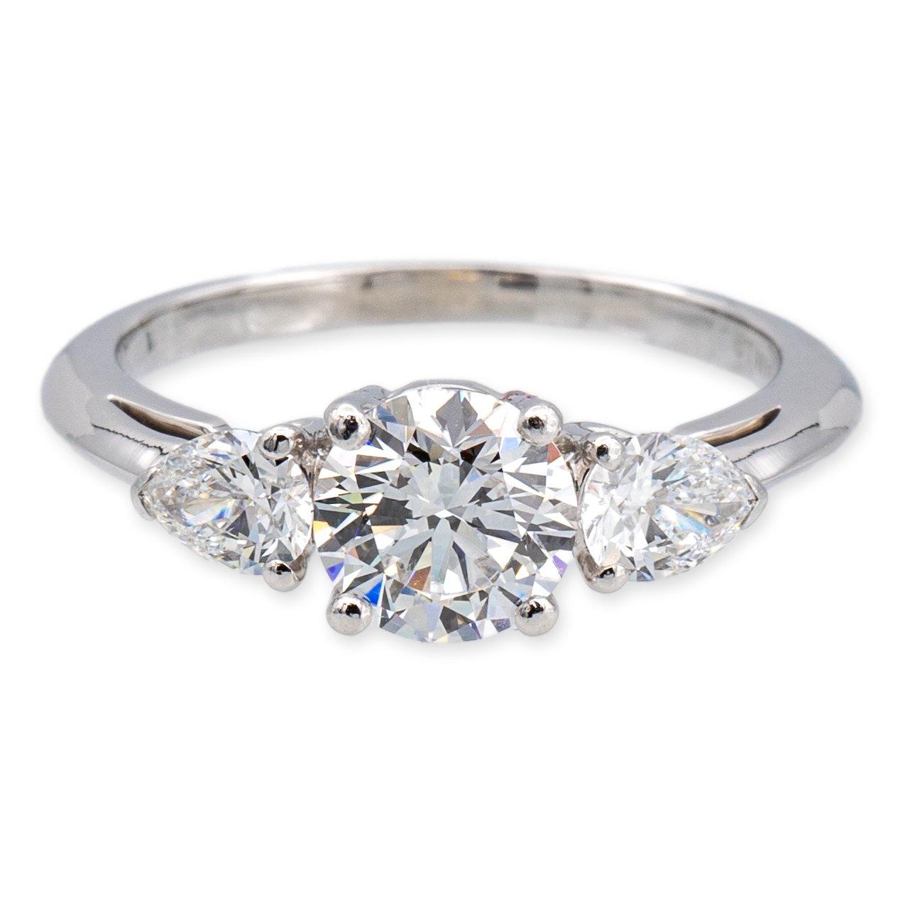 Tiffany & Co. classic three stone engagement ring finely crafted in platinum featuring one round brilliant cut diamond center and two pear shaped side stones set in an open gallery design. The center diamond weighs 1.06 carats , very fine E color