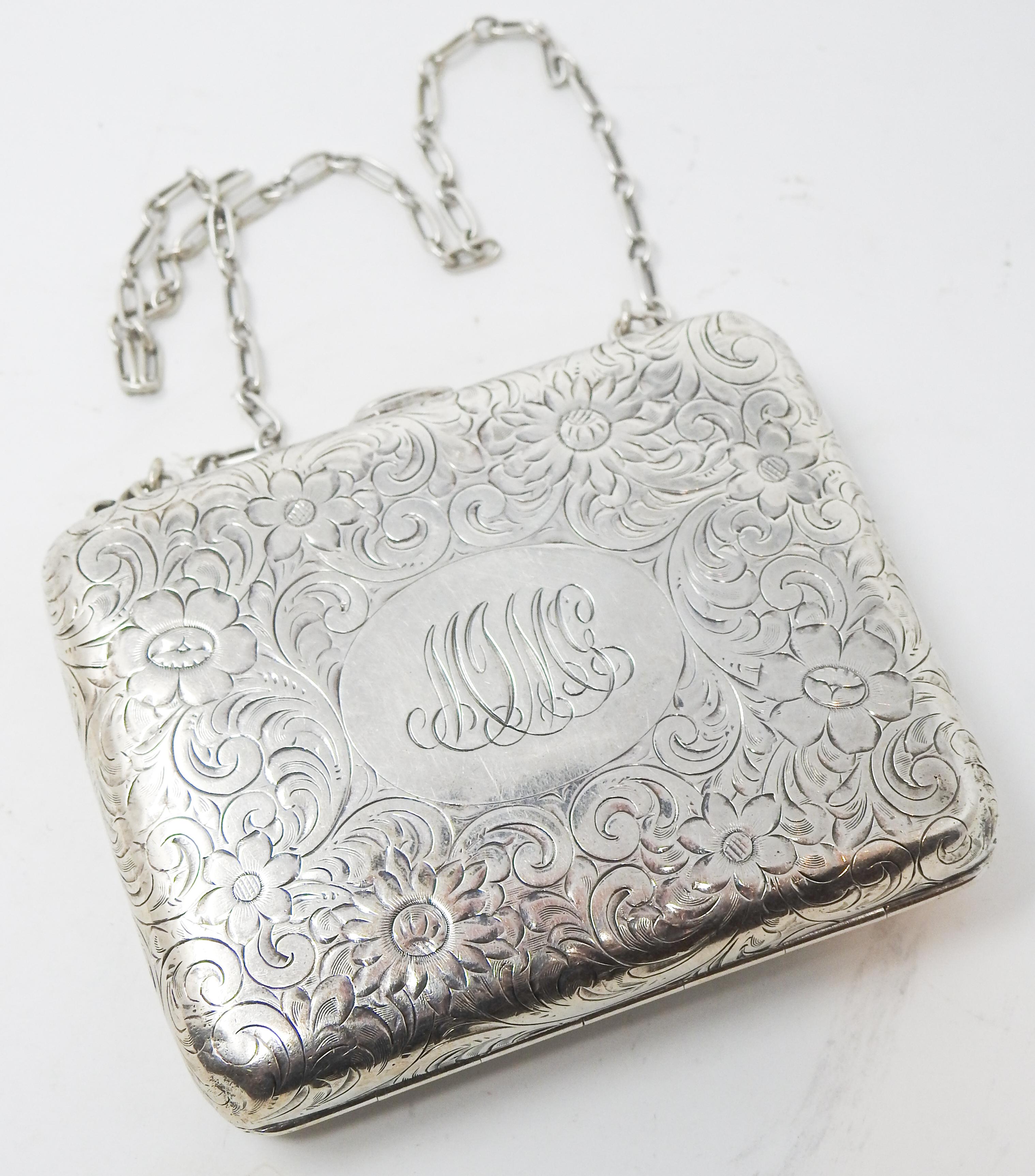 Offering this elegant sterling silver change purse Made for Tiffany & Co. The purses body is covered in floral, foliate, and scrollwork engraved filigree. On the front there is an oval in the center with the initials MJMcC. There is a simple chain,