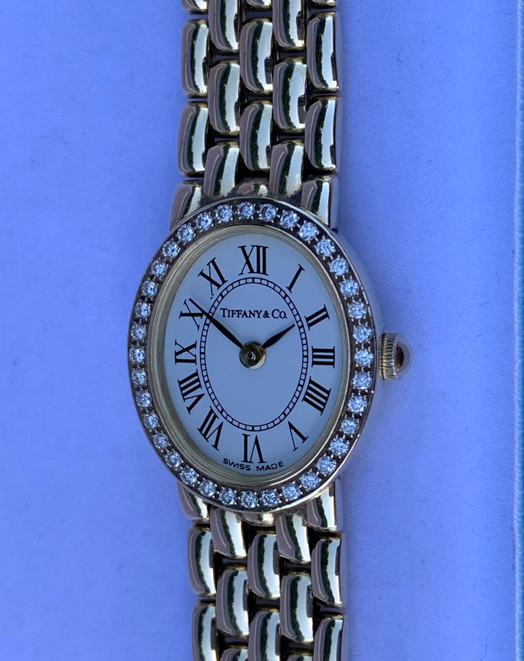Finest quality designer Tiffany & Company quartz movement oval face ladies wrist watch in 14 karat yellow gold features a beautiful diamond bezel and a 14 karat yellow gold link bracelet. The watch has a solid gold oval case with a small gold crown
