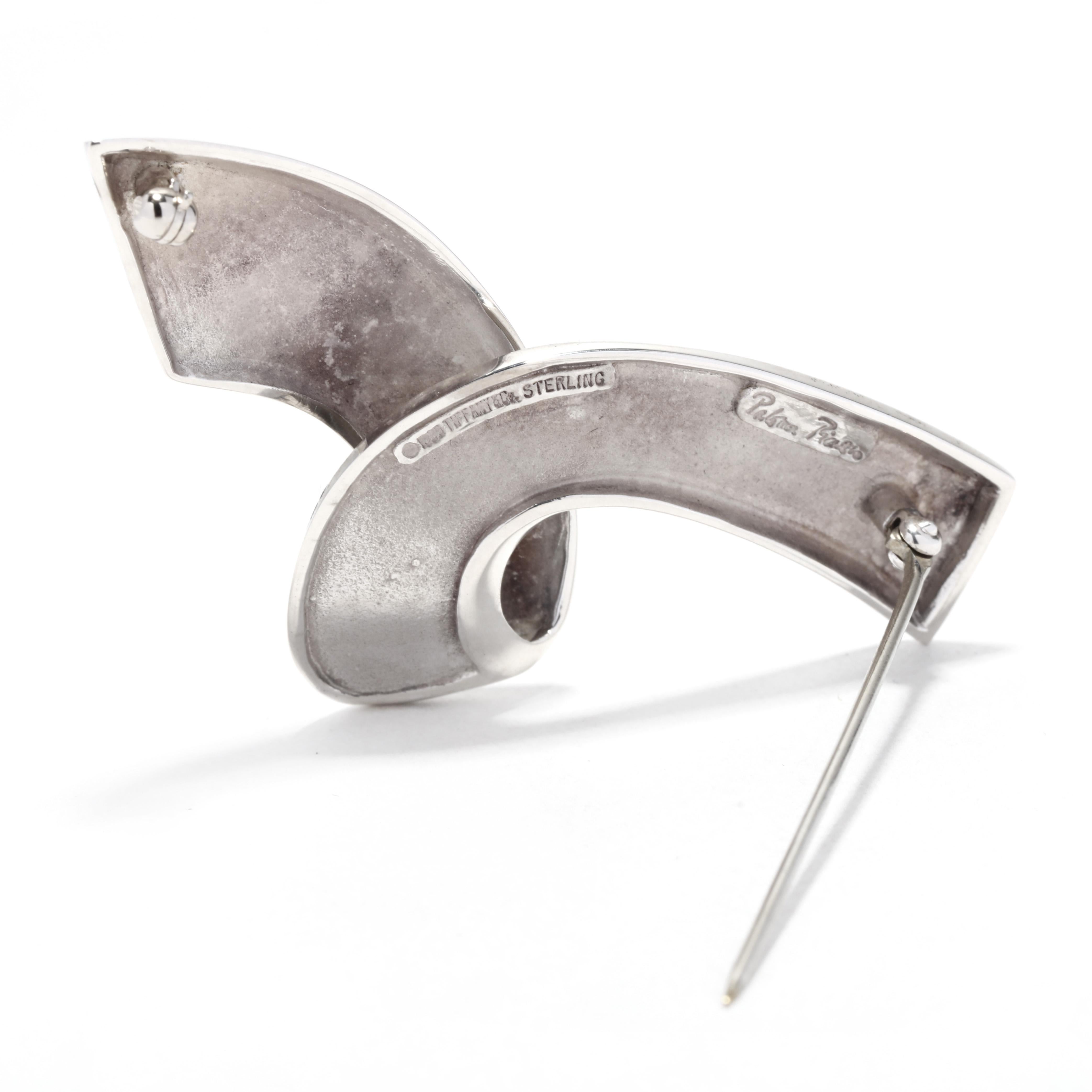 A vintage Tiffany and Company Paloma Picasso sterling silver ribbon brooch. This large silver brooch features a flat ribbon motif with a folder over in the center and with a pin stem C clasp.

Length: 2 1/8 in.

Width: 1 in.

Weight: 6.9 dwts. /