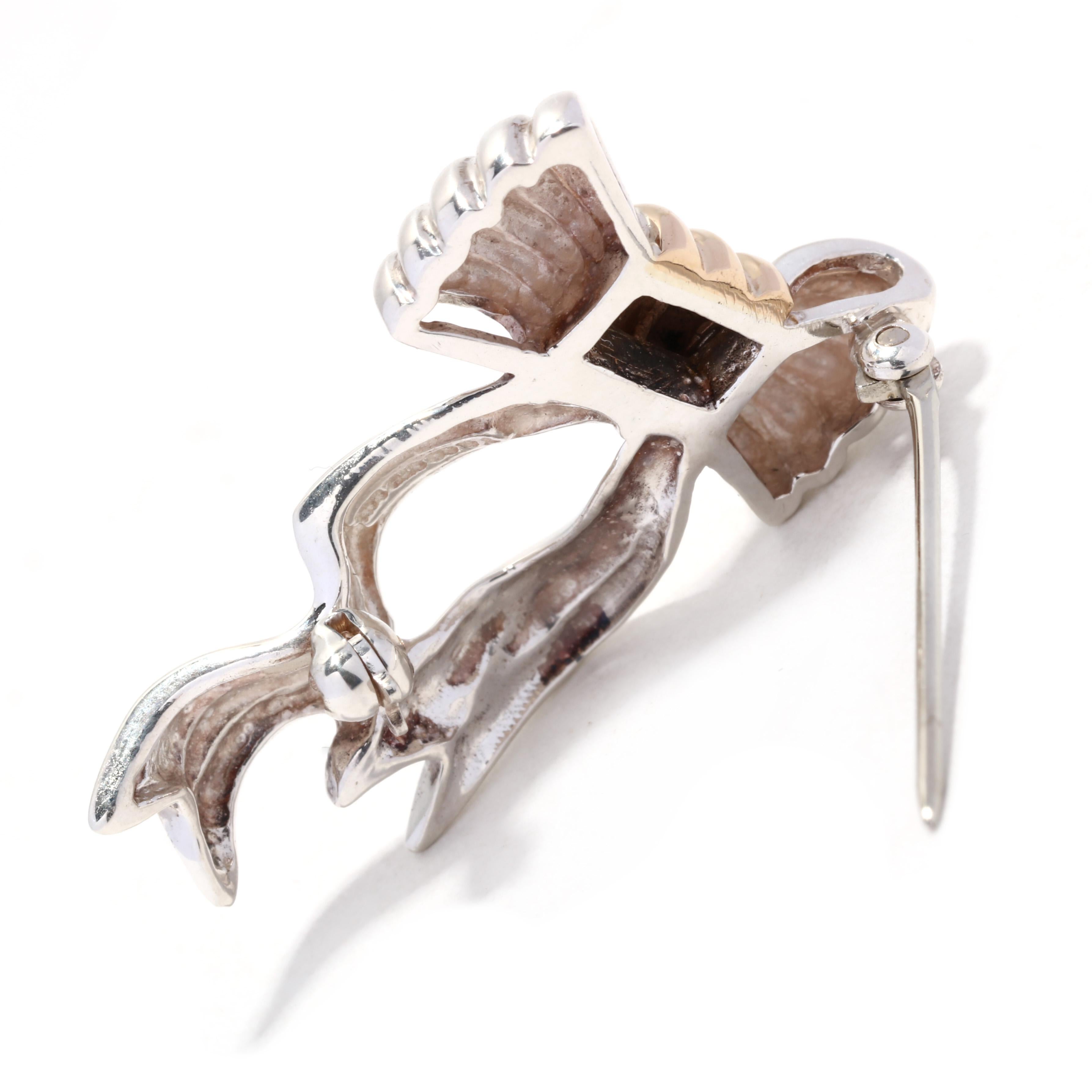 A vintage Tiffany and Company 18 karat yellow gold and sterling silver small bow brooch. This simple bow brooch features flowing box motif with a central yellow gold knot and with ridged detailing.

Length: 1 1/8 in.

Width: 5/8 in.

Weight: 3.3