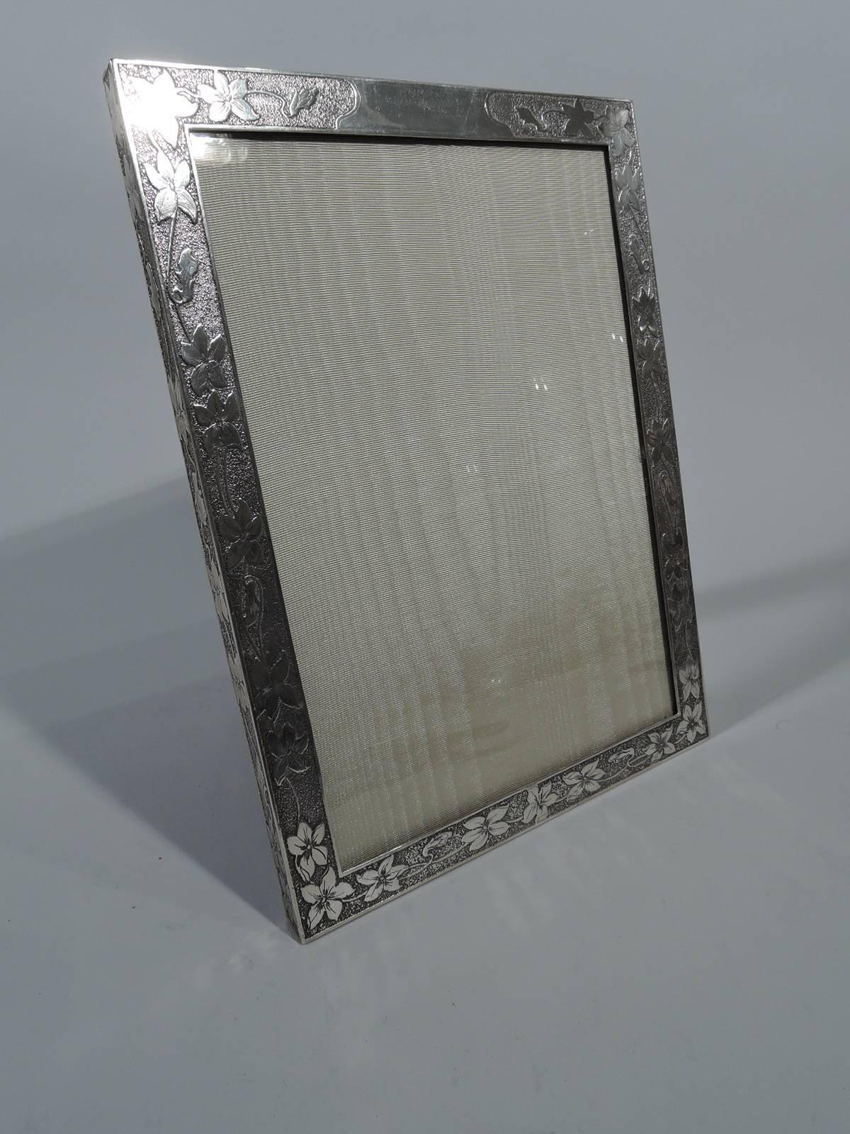 Art Nouveau sterling silver frame. Made by Tiffany & Co. in New York. Rectangular window bordered by acid-etched and engraved flowers (possibly morning glories) on stippled ground. Same on sides and top edge. Shaped cartouche (vacant). For portrait