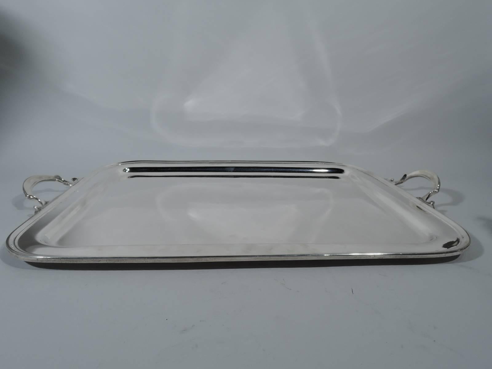 Classic sterling silver tea tray. Made by Tiffany & Co. in New York. Rectangular with round corners and molded rim. End bracket handles scrolled with stylized leaf mounts. Restrained and functional in the Modern style, though also goes with the