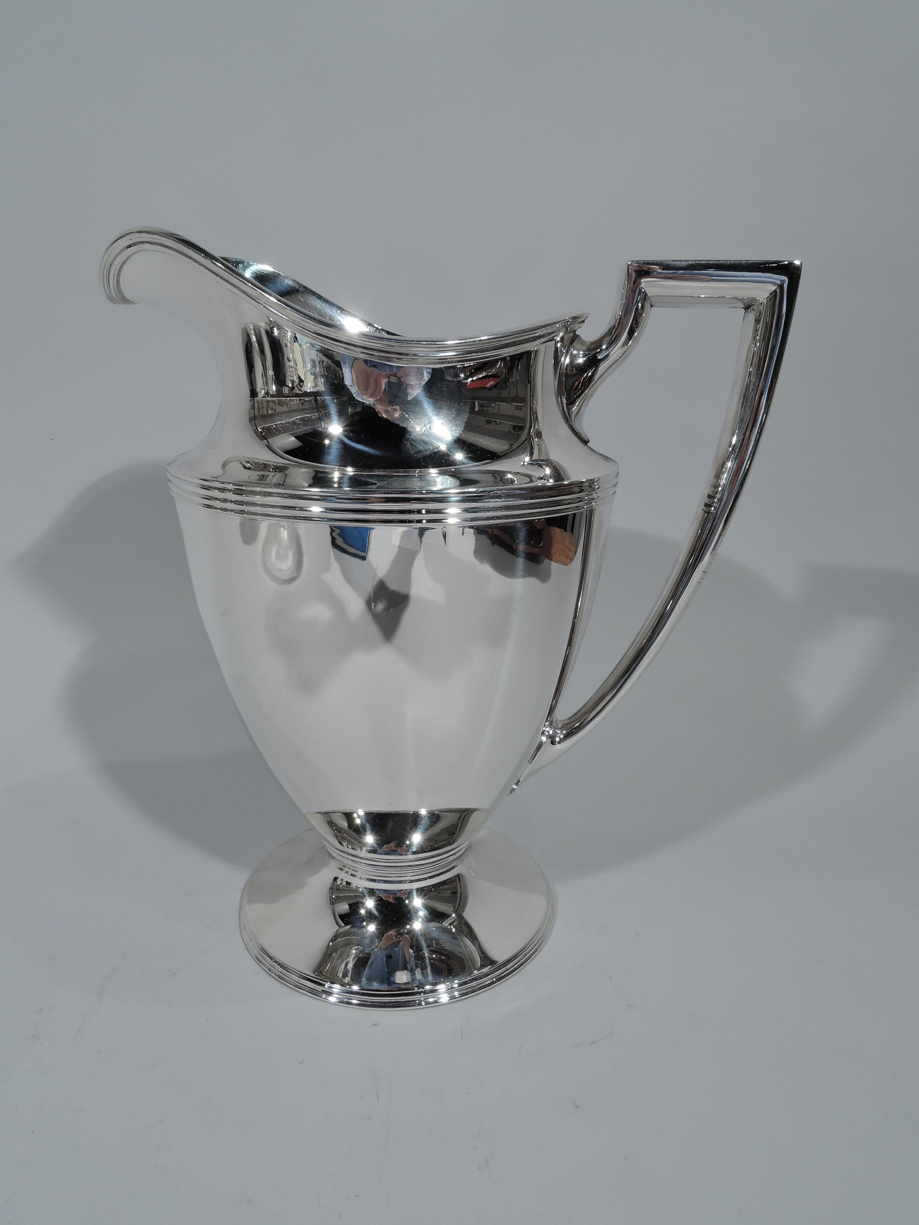 Classic sterling silver water pitcher. Made by Tiffany & Co. in New York. Curved and tapering body, raised and stepped foot, scrolled bracket handle, and helmet mouth. Ornamental reeding. Fully marked including pattern no. 18181, director’s letter M