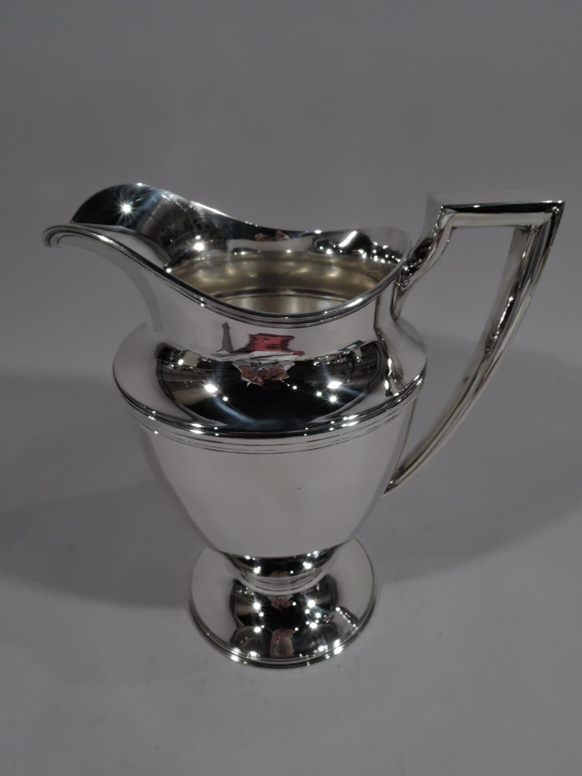 Classic sterling silver water pitcher. Made by Tiffany & Co. in New York. Curved and tapering body, raised and stepped foot, scrolled bracket handle, and helmet mouth. Reeding. Fully marked including pattern no. 18181, director’s letter m