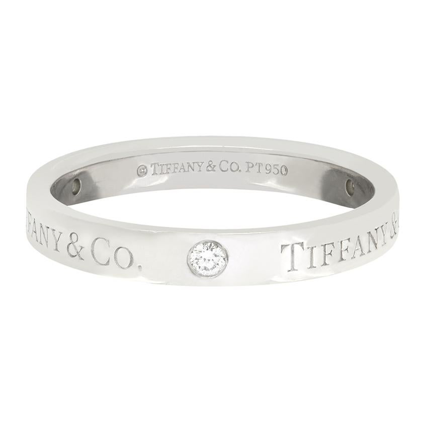 Cette magnifique alliance est proposée par le créateur Tiffany & Co. Fabriqué en platine et d'une largeur de 3 mm, ce bracelet est de forme plate avec le nom du créateur et trois diamants sertis par frottement. Les diamants totalisent 0,07 carat et