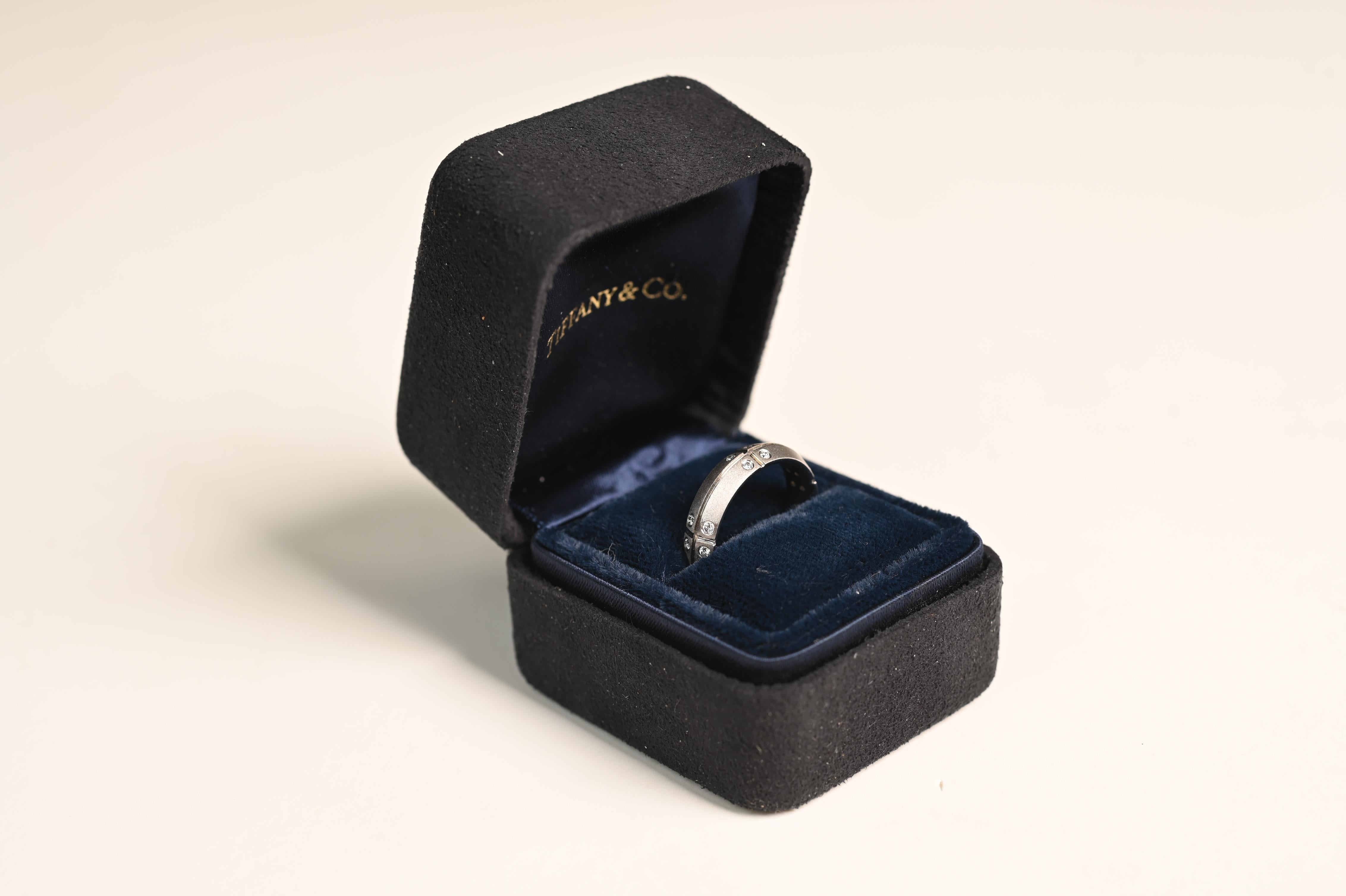 This exquisite Tiffany & Co. wedding band is masterfully crafted in 18k white gold, featuring a sophisticated design adorned with round brilliant-cut diamonds. A distinctive horizontal groove encircles the band, intersected by evenly spaced vertical