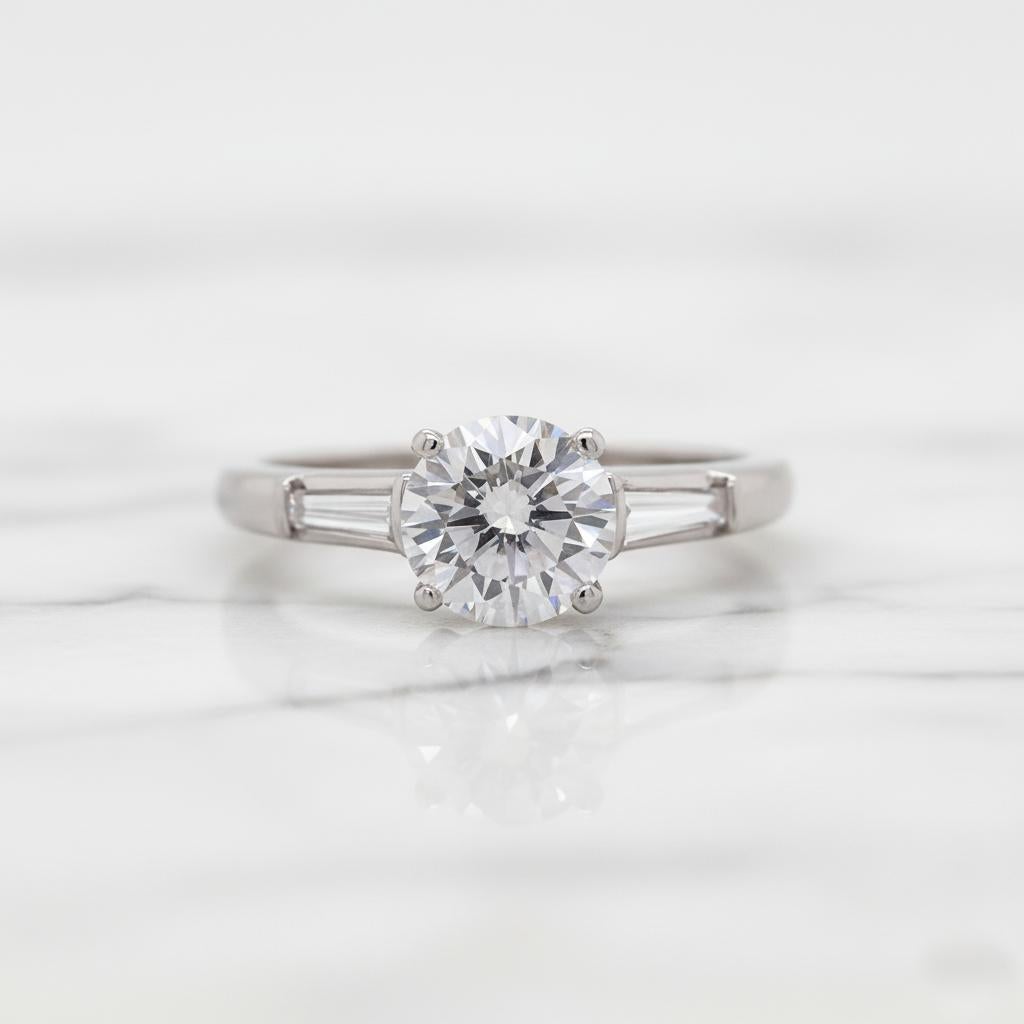 Exemple exquis du savoir-faire intemporel de Tiffany & Co., cette bague de fiançailles à trois pierres en platine met en valeur un superbe diamant rond brillant de 1 carat d'une qualité exceptionnelle. De couleur G et de pureté VVS2, la pierre