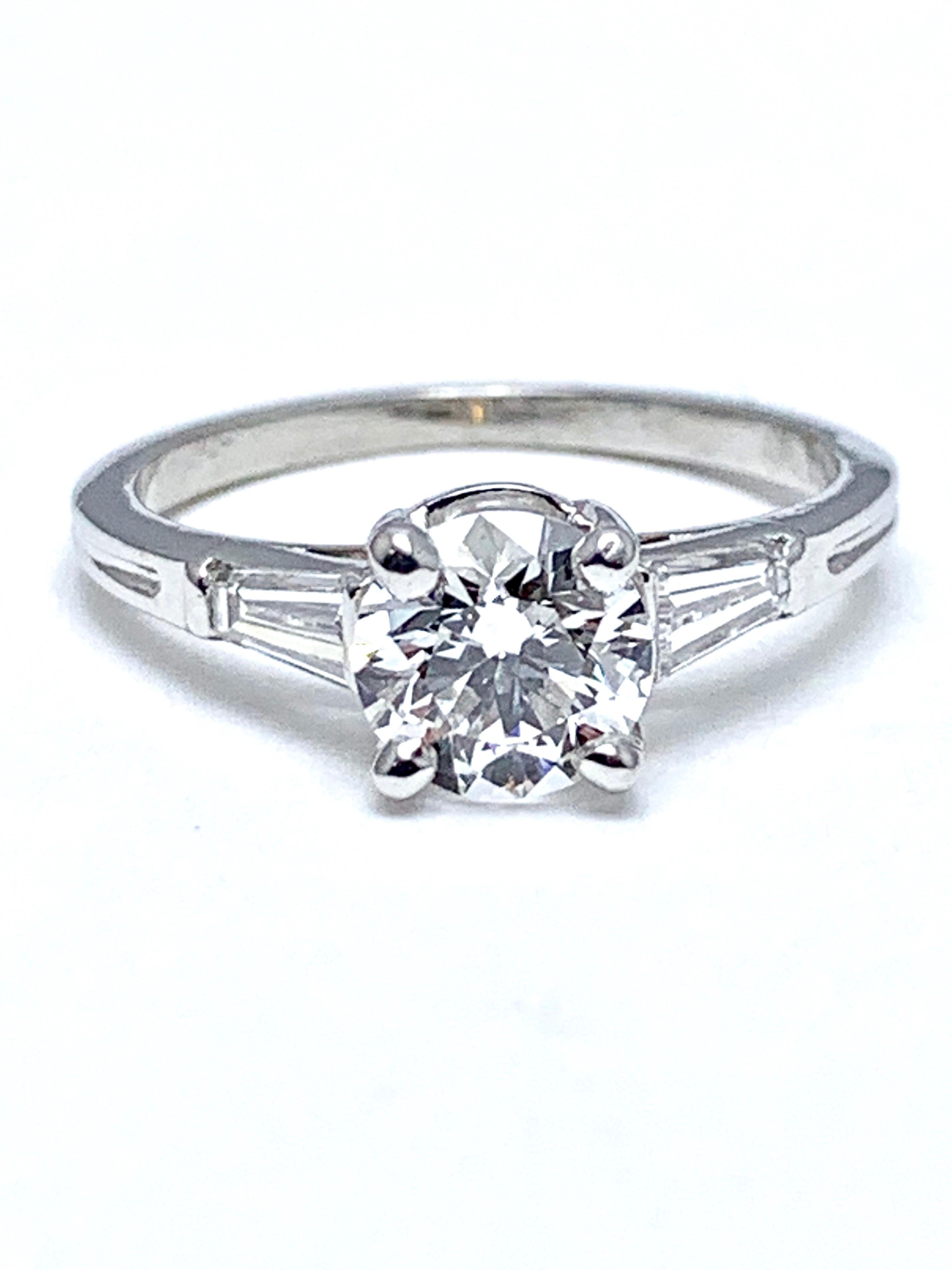 A fiery Tiffany & Co. 1.05 carat round brilliant Diamond and tapered baguette Diamond platinum engagement ring.  The center Diamond is set in a four prong basket setting, with two tapered baguettes leading into the shank of the ring.  The 1.05 carat