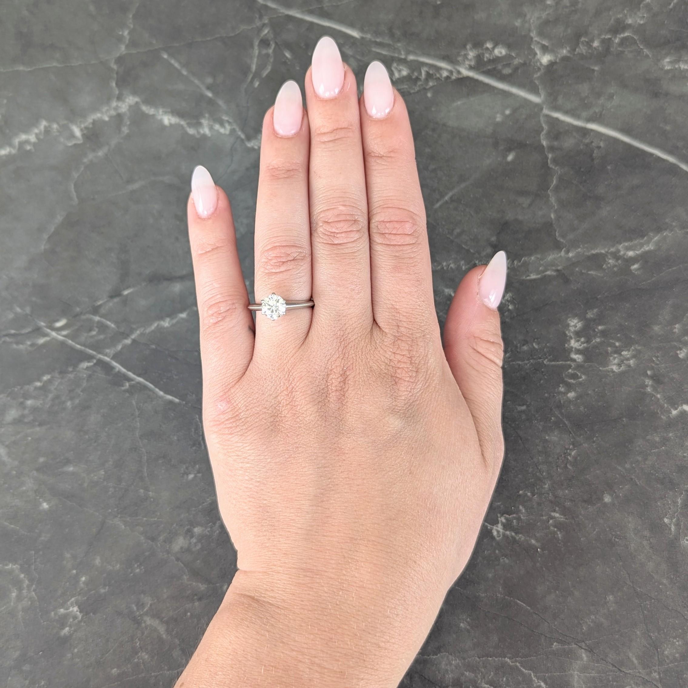 Centering a round brilliant cut diamond weighing 1.11 carats - I color with VS1 clarity
Set in a six pronged classic Tiffany style mounting
Flanked by knife edge shoulders
Inscribed with carat weight
Stamped for platinum
Numbered and fully signed