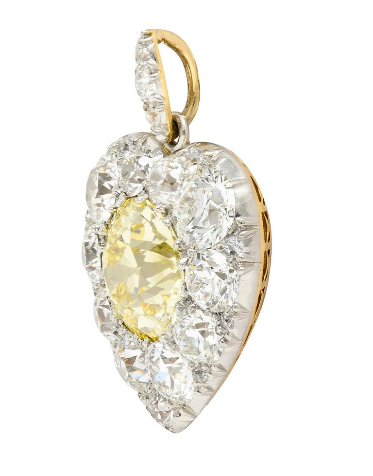 Designed as a platinum-topped heart shape centering an old European cut diamond. Weighing 6.12 carats total natural fancy yellow in color with VS1 clarity. Bead set with a clustered surround of old European cut diamonds. With additional diamonds in