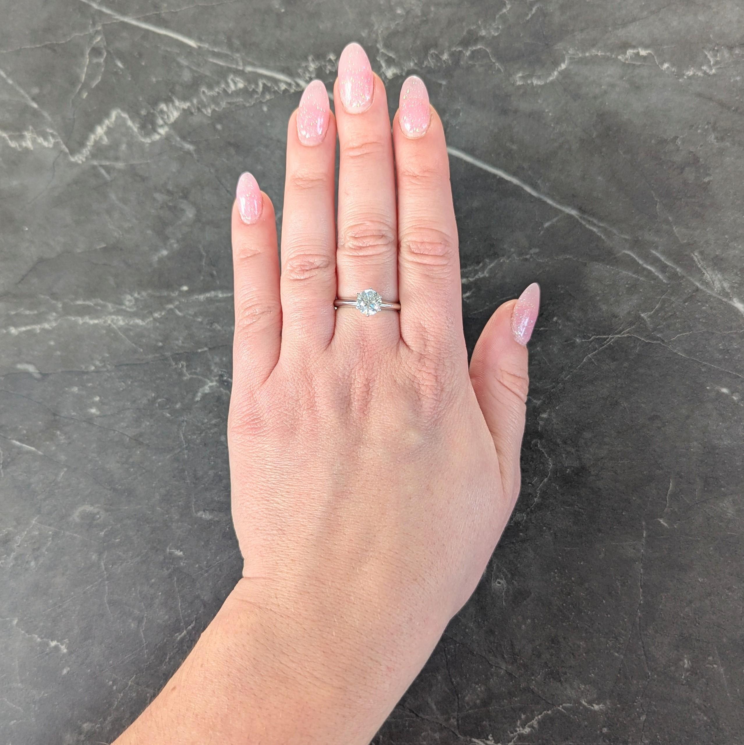 Centering a round brilliant cut diamond weighing 1.29 carats - I color with VS1 clarity
Set in a six pronged classic Tiffany style mounting
Flanked by knife edge shoulders
Inscribed with carat weight
Stamped for platinum
Numbered and fully signed