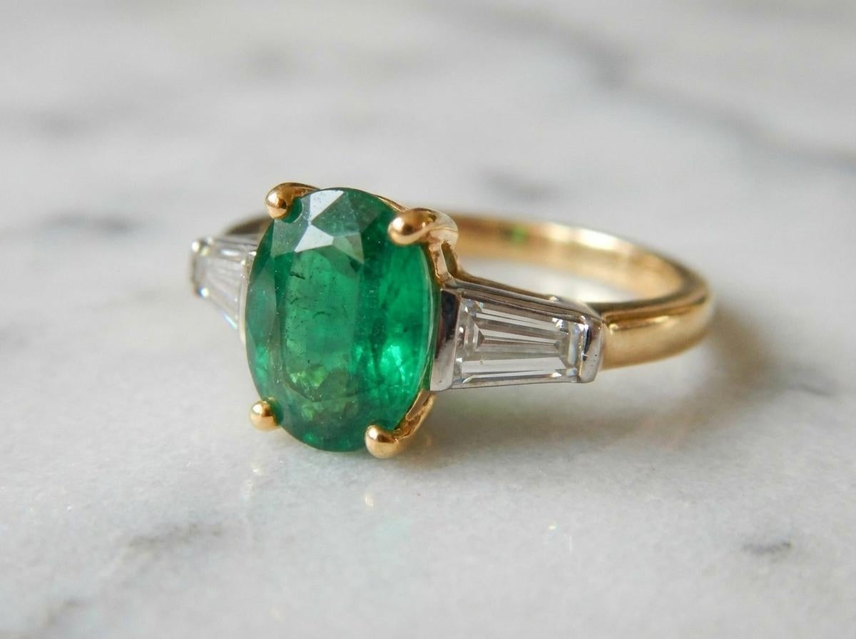 Cette élégante bague Tiffany & Co. présente une émeraude de 1,30 carat sertie dans un riche or jaune 18 carats, accentuée par deux diamants baguettes effilés totalisant environ 0,43 carat. Les diamants sont de couleur G-H et de pureté VS, offrant un