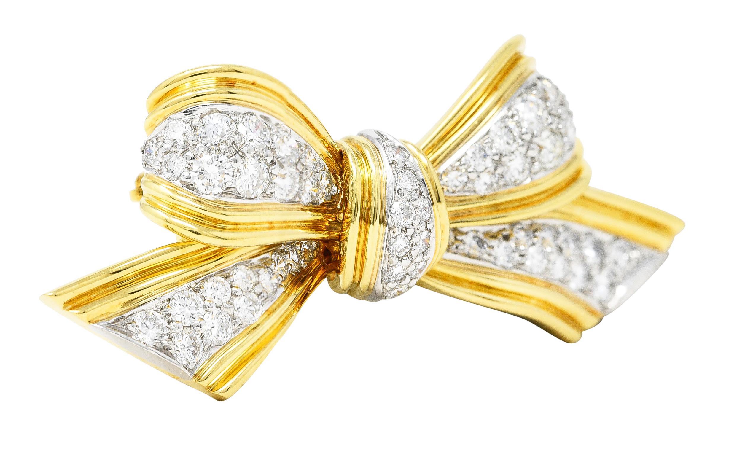 Designed as a bow comprised of ridged gold ribbon with round brilliant cut diamonds. Weighing approximately 1.30 carats total - G/H color with VS clarity. Pavé set in platinum segments. Completed by hinged pin stem with locking closure. Stamped for