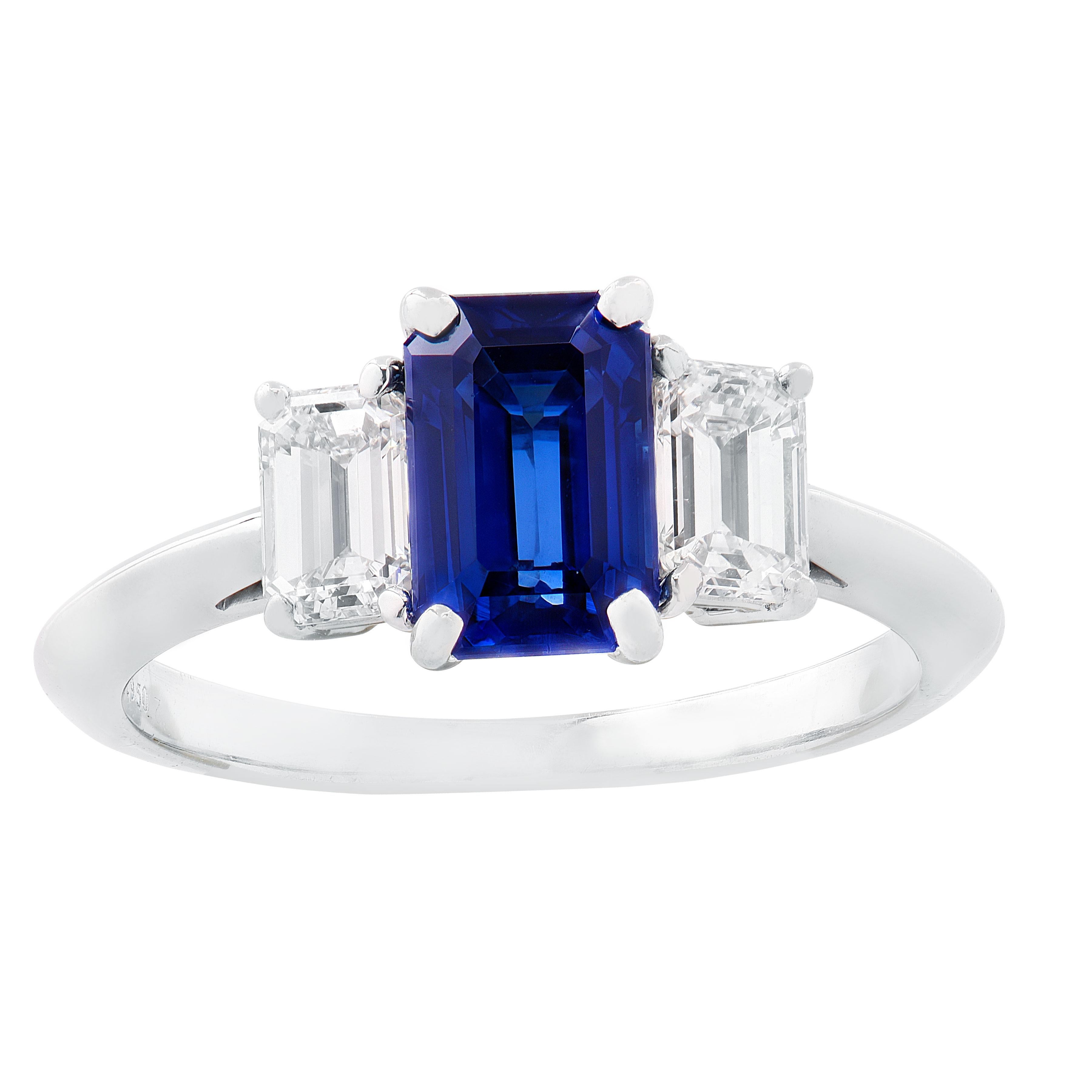 Cette bague intemporelle à trois pierres de la maison Tiffany & Co. est réalisée en platine et met en valeur un saphir bleu de taille émeraude pesant environ 1,35 carat. La pierre centrale est flanquée de deux diamants taille émeraude d'un poids