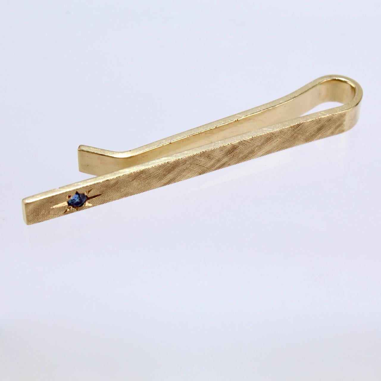 A handsome Tiffany & Co. tie clip in 14K gold in a refined size.

The thin tie bar features a wheel engraved cross hatch pattern and is set with a small round cut sapphire.  

Eye catching Mid-Century design from Tiffany!

Date:
Mid-20th