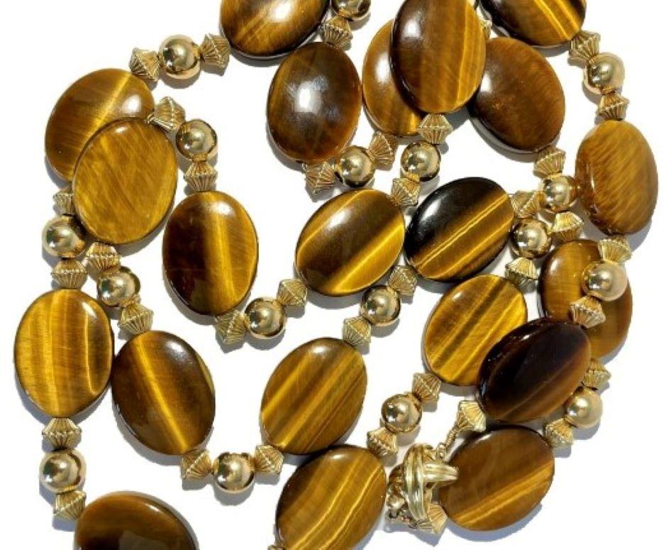 This very pleasing 14k yellow gold Tiffany neck chain is comprised of twenty one natural oval quartz tiger's eye slabs, all separated by sets of three 14k fluted and polished beads.  It features an iconic Tiffany 