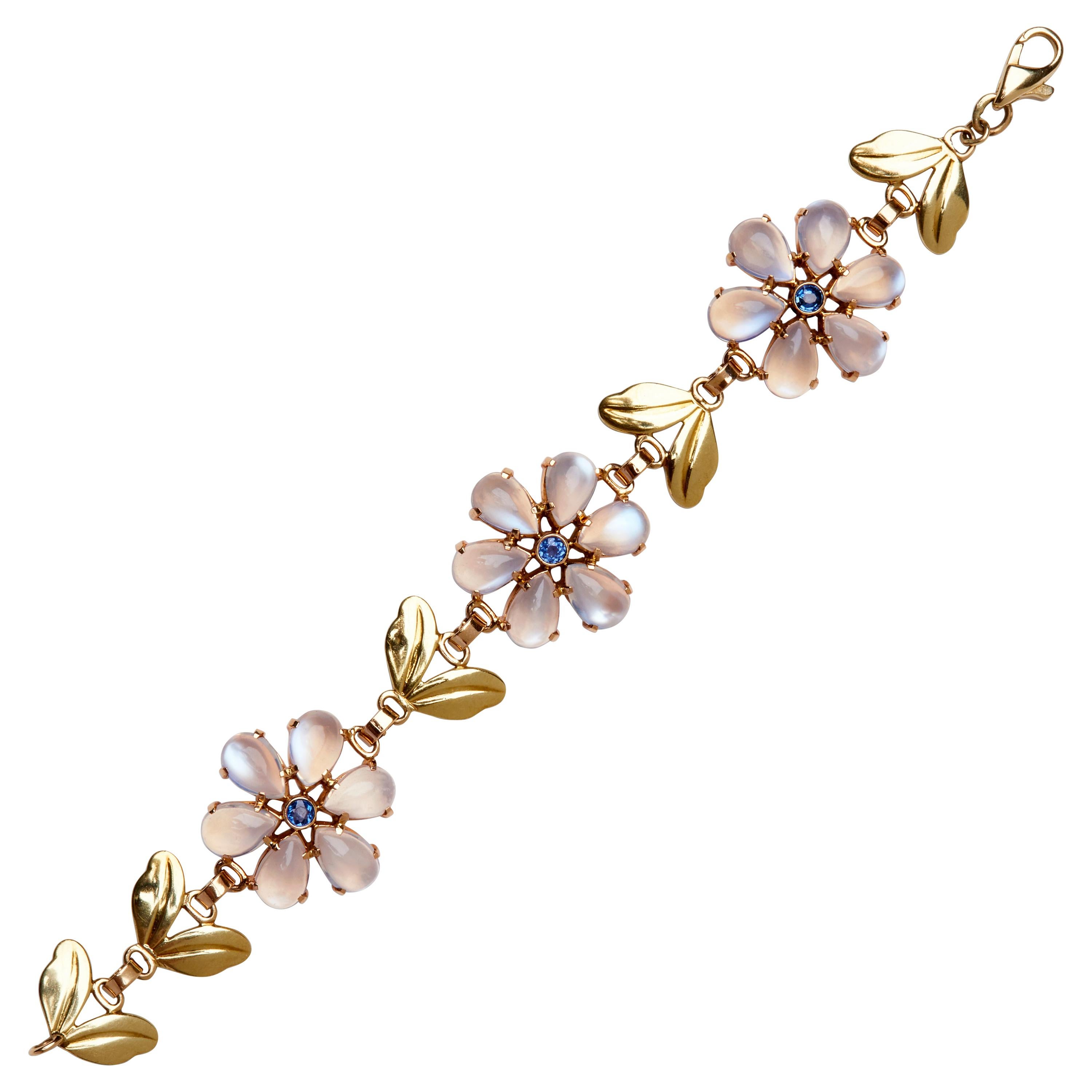 Dieses elegante Armband von Tiffany & Co. aus den 1940er Jahren zeigt drei Stationen mit Blumenmotiven, die durch blattförmige Glieder getrennt sind. Jede Blüte besteht aus leuchtenden Cabochon-Mondsteinblütenblättern, die von blauen Saphiren im