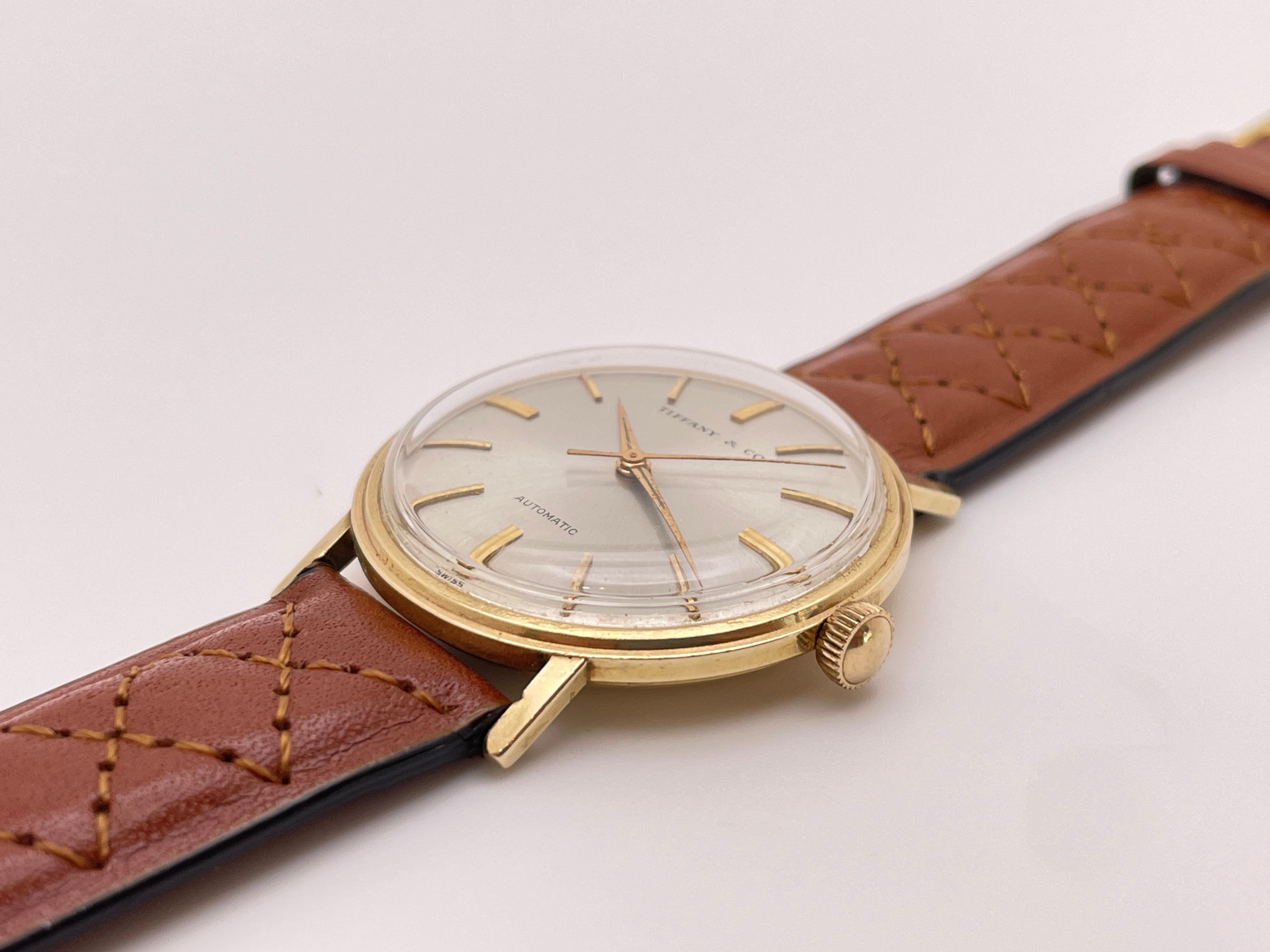 A vintage 14K yellow gold Tiffany & Co. automatic watch. Featuring a round 14K yellow gold case, champagne dial, gold tic marks, sharp gold hands, and automatic movement. Brown leather band.

This beautiful, classic watch has a 34 mm case diameter,