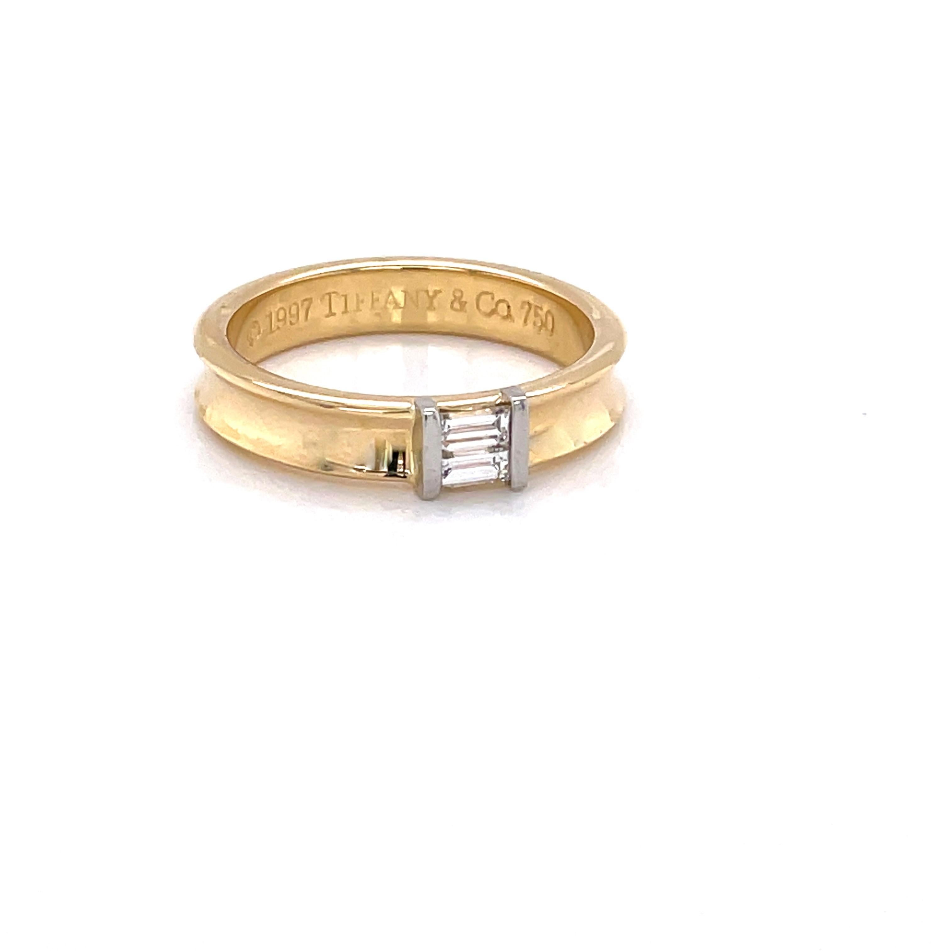 Two straight faceted cut baguette G/VS diamonds, .24 carat total weight, are center stage and set horizontally on this elegant 4.5mm contoured band ring of
 eighteen karat 18K yellow gold by Tiffany & Co. In ring size 10 and sizable. Stamped 750 and