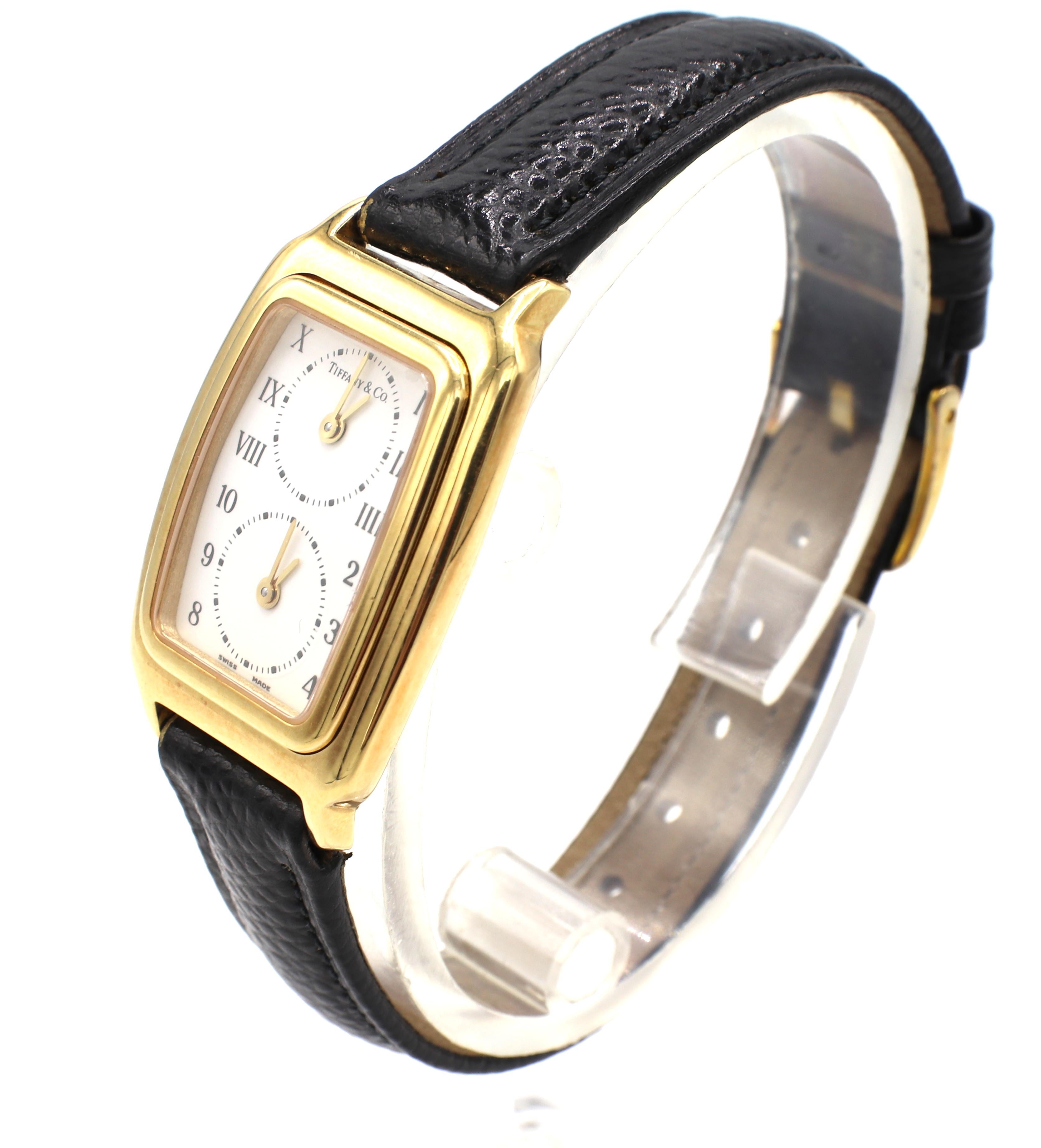Tiffany & Co. 18 Karat Gold Dual Time Zone Watch
Metal: 18k yellow gold
Weight: 29.2 grams
Band: Black leather
Dial: White
Case: 18k yellow gold, hinged pop-out 22 x 34mm
Model: L203
Water resistant
Movement: Quartz
Crystal: Sapphire
Signed: