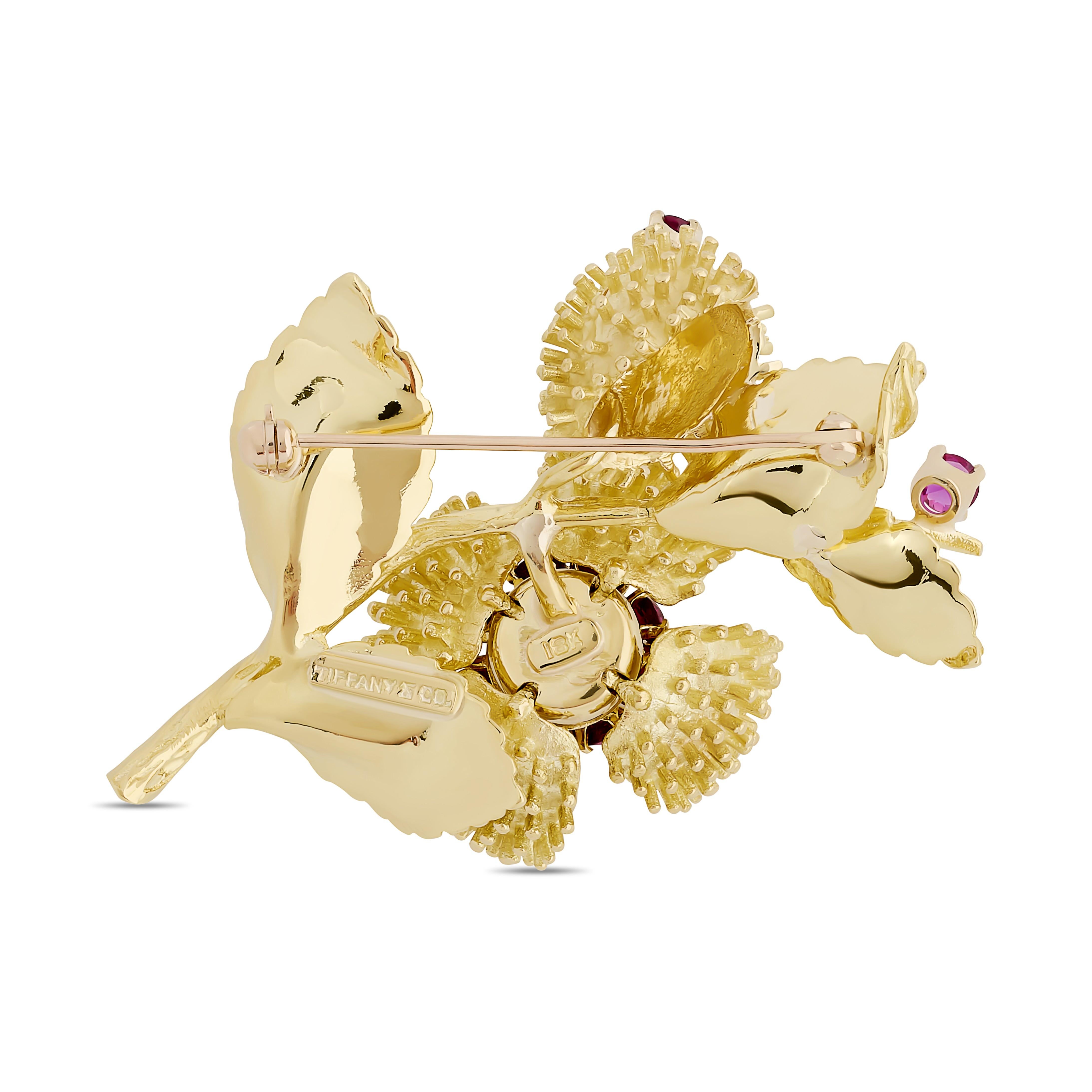 Diese exquisite Anstecknadel aus 18-karätigem Gelbgold von Tiffany & Co. ist mit leuchtenden Rubinen im Rundschliff besetzt, die einen zentralen Diamanten umgeben. Ein beweglicher Branch, der mit zusätzlichen Rubinen akzentuiert ist, sorgt für einen