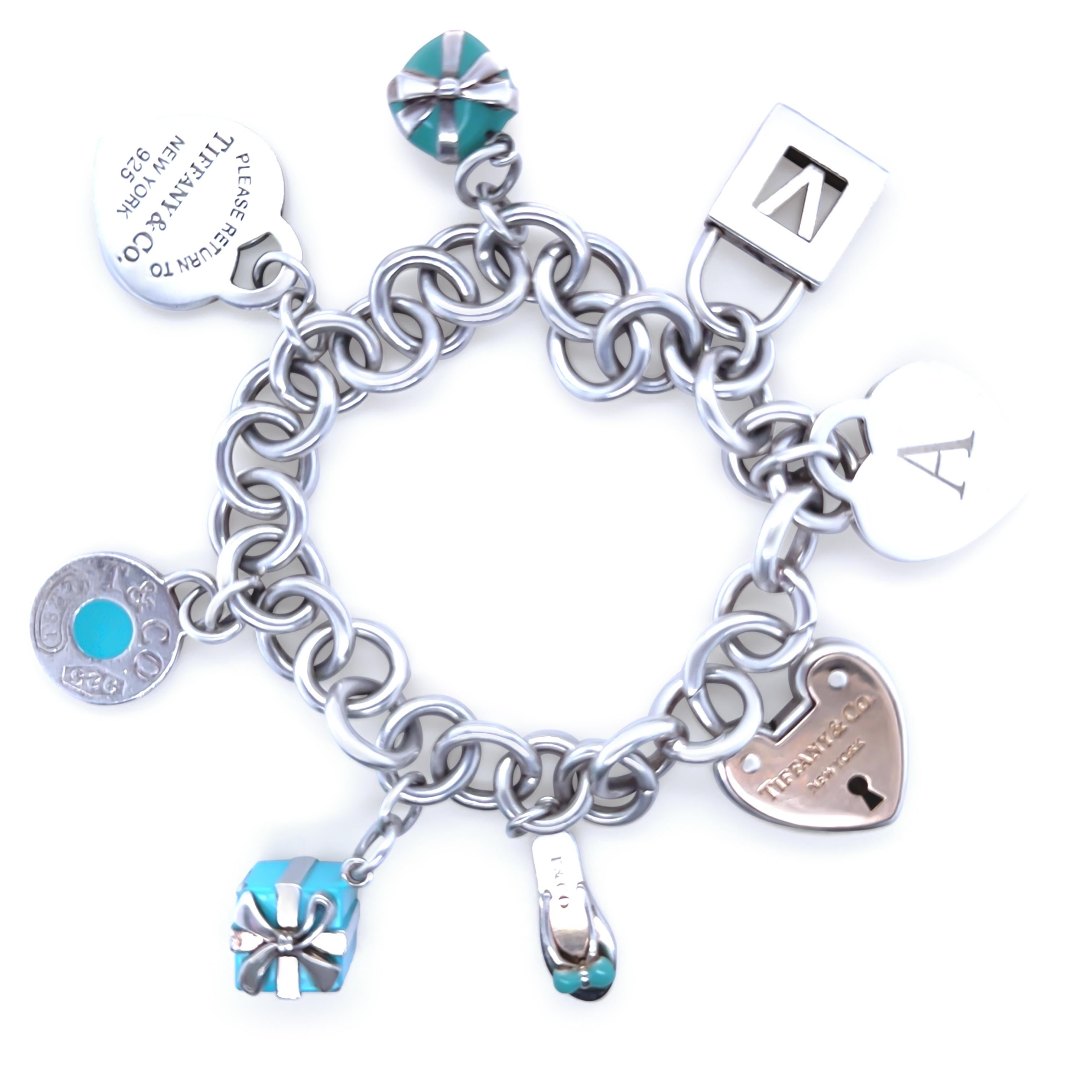 This iconic Tiffany & Co. charm bracelet beautifully combines sterling silver and 18ct yellow gold, weighing a total of 78.7 grams. The bracelet is adorned with eight enchanting charms, including a heart charm engraved with the letter “A,” a letter