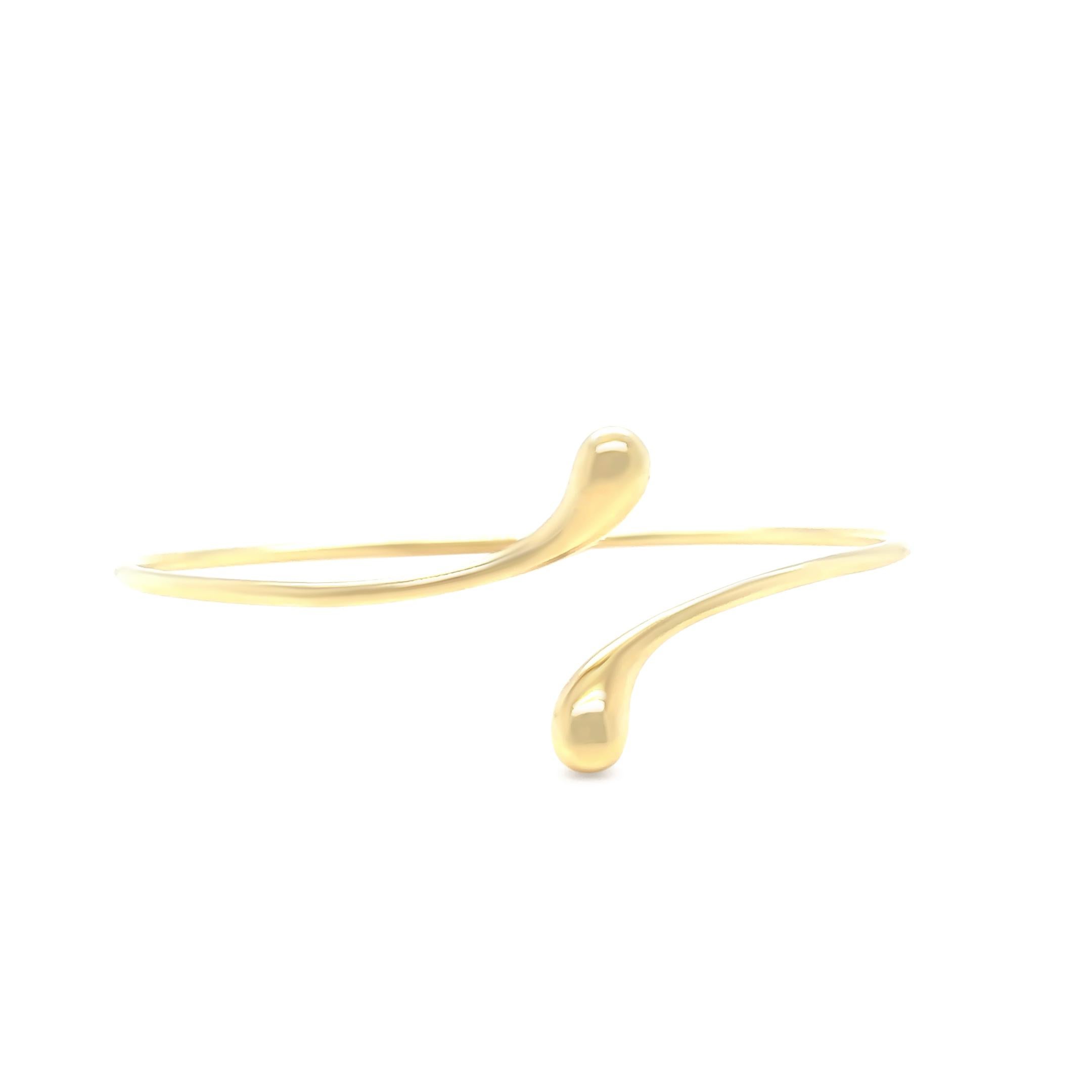 An authentic Tiffany & Co bangle crafted in 18ct yellow gold, designed by the iconic Elsa Peretti. This elegant piece features her signature elongated teardrop shape, reminiscent of a solitary raindrop or shining bead of morning dew.

Measuring