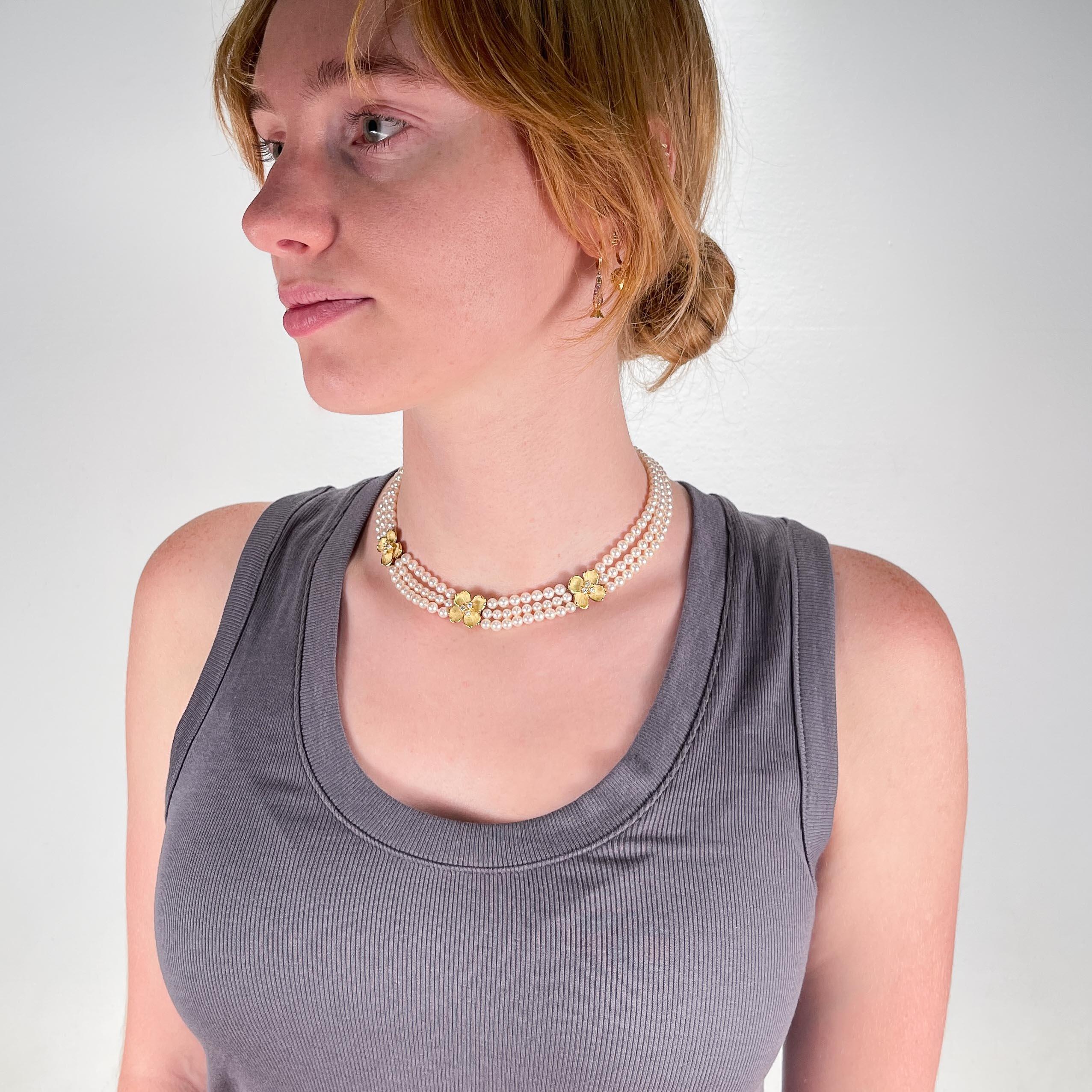 A very fine gold, diamond and pearl 'Dogwood' necklace. 

By Tiffany & Co. 

In 18k yellow gold.

With three strands of 4.5-5mm cultured pearls, three sculpted gold dogwood blossoms centered on a round cut diamond cluster pistil, and a conforming