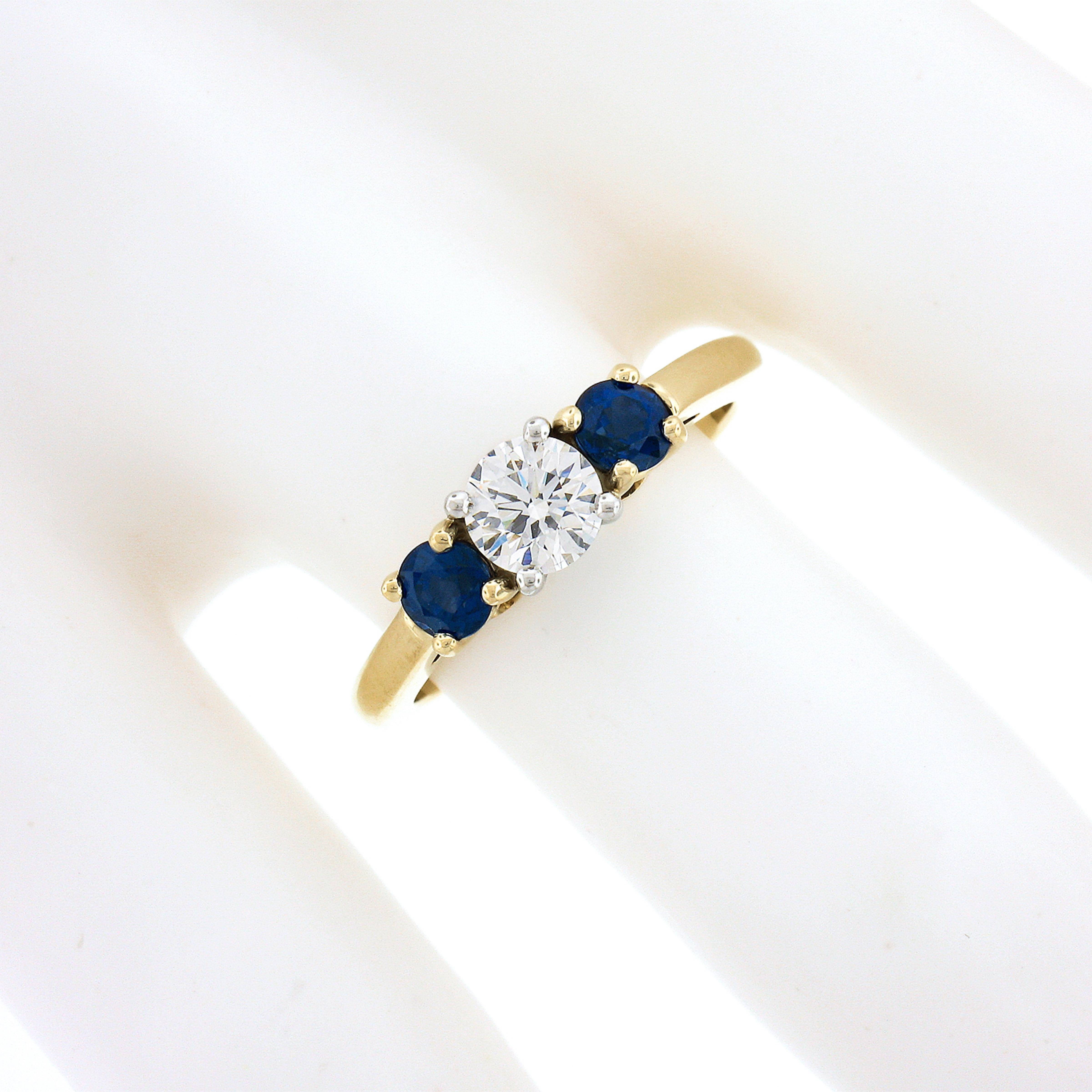 You are looking at a stunning diamond and sapphire, all original, Tiffany & Co. ring crafted in solid 18k yellow gold featuring an elegant three-stone style across its top. The gorgeous fine diamond solitaire is neatly prong set at the center in