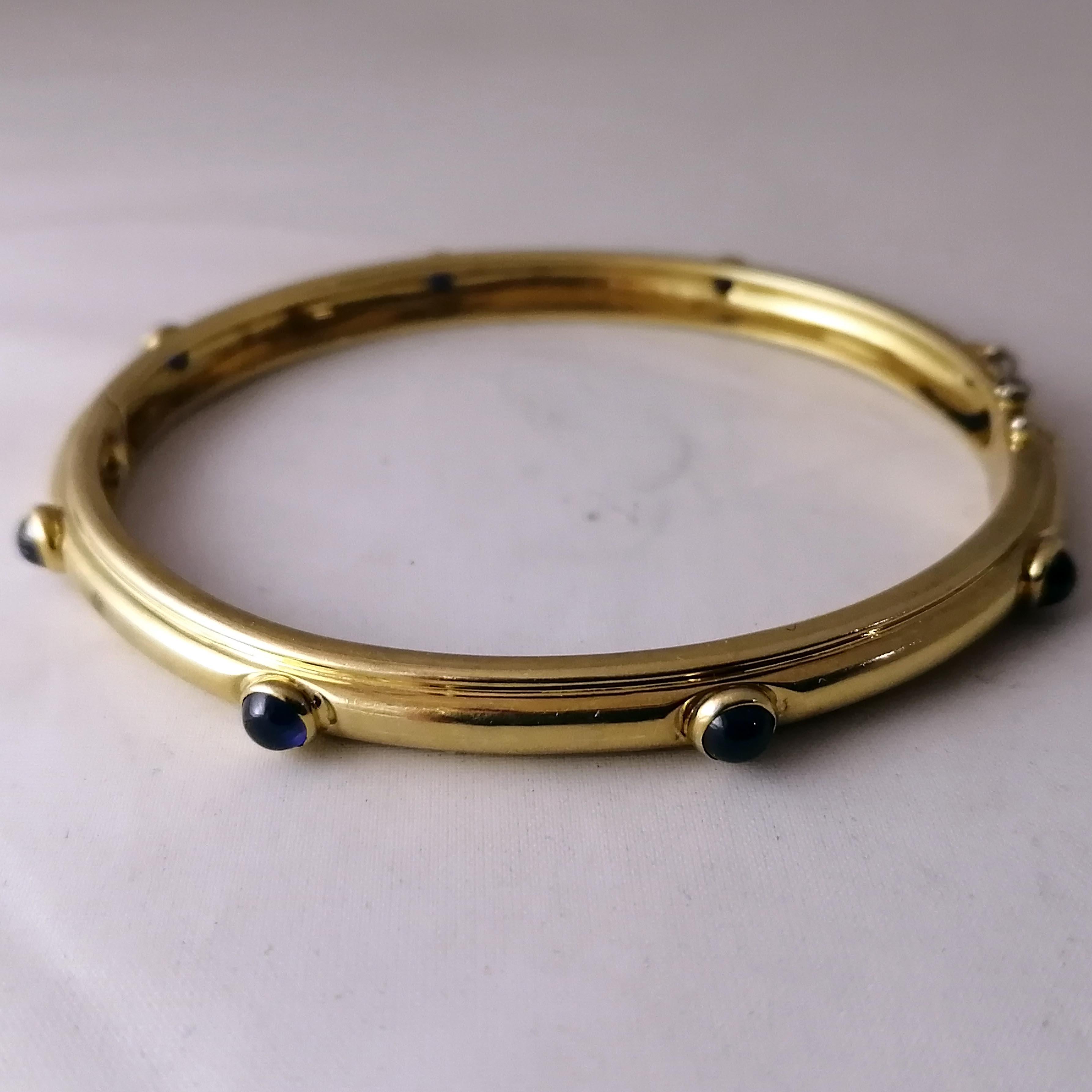 A fabulous Italian made 18-karat gold and sapphires bangle bracelet by Tiffany & Co. The hinged bangle has 8 bezel set cabochon sapphires and safety chain. The piece is marked on the interior with the Tiffany & Co. logo, the 750 mark and the ITALY