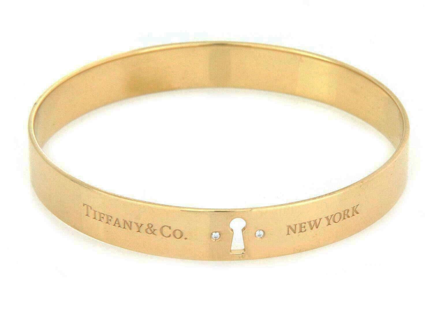 This elegant large size authentic bangle is by Tiffany & Co. from the Keyhole Lock Collection. It is crafted from 18k yellow gold with a polished finish featuring a 9mm wide band bracelet.  The front center of the bangle has a keyhole with a flush