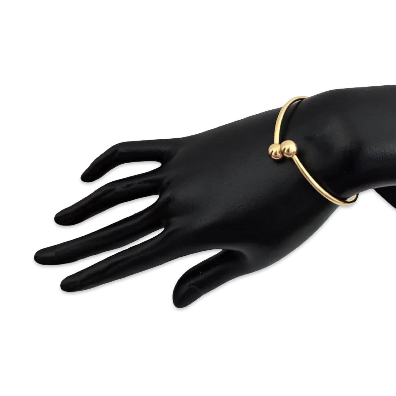 Minimalista e inconfondibilmente raffinato, questo autentico braccialetto aperto in oro giallo 18 carati di Tiffany & Co. presenta due sfere lucide di circa 7,65 mm ciascuna. Il braccialetto ha un diametro interno di circa 1,96 pollici (≈50 mm) e si