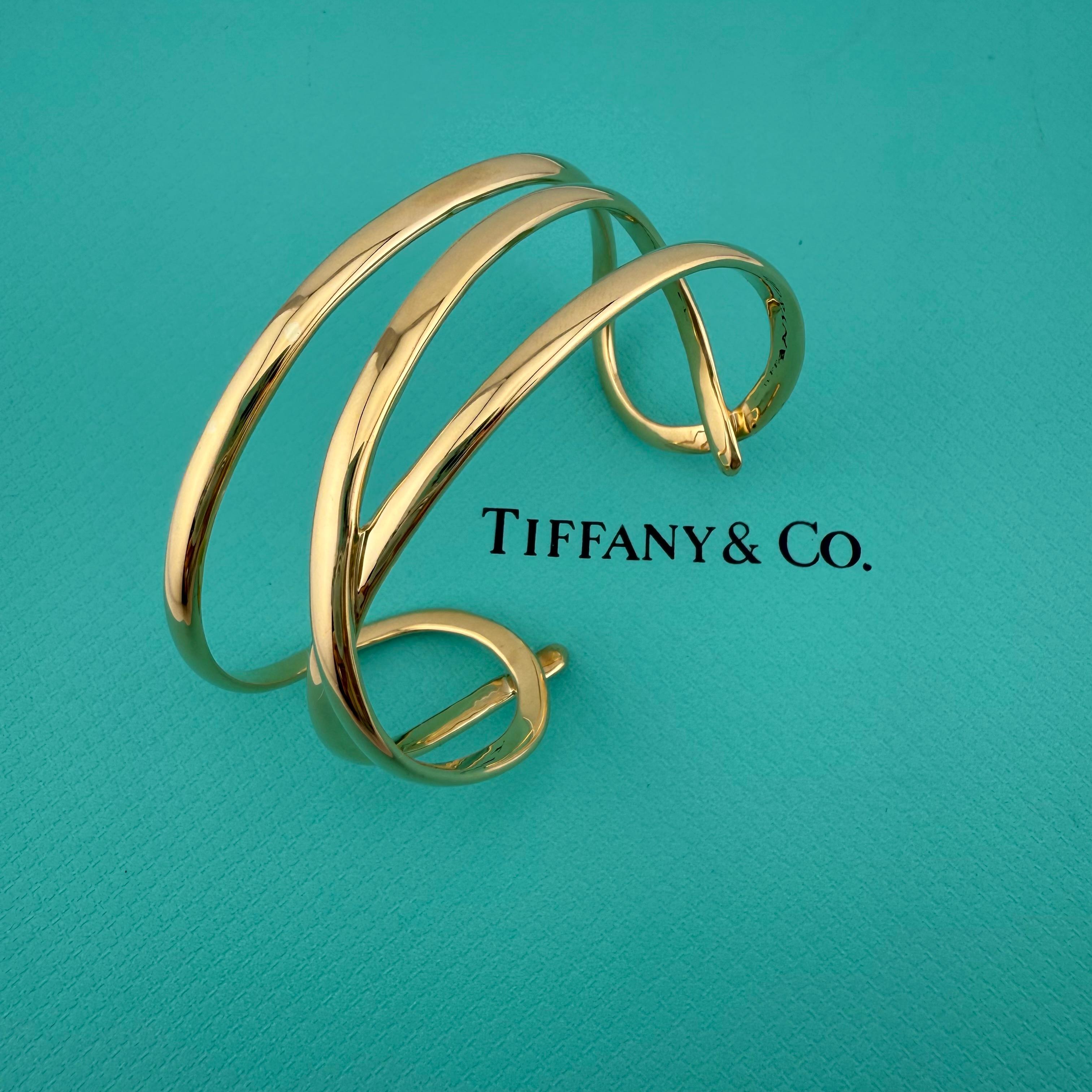Tiffany & Co Looping Cuff Bracelet circa 1980's
Le style :   Bracelet
Métal :  Or jaune 18kt / 750
Poids :  47,7 grammes
Taille :  6.75' pouces
Largeur :  1' pouce
Hallmark :  ©1980TIFFANY&CO. 750
Comprend :   A.I.C. Pochette à bijoux