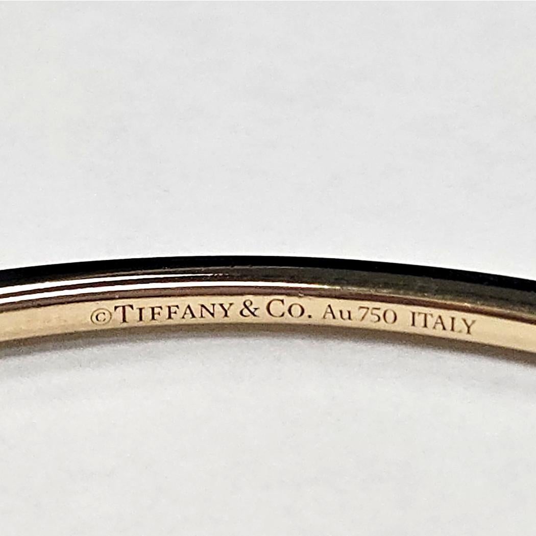 Questo squisito bracciale di Tiffany & Co. incarna un minimalismo raffinato e un'eleganza duratura. All'interno dell'elegante struttura bangle in oro giallo 18 carati si nasconde una fila continua di circa 45 diamanti taglio brillante, per un totale