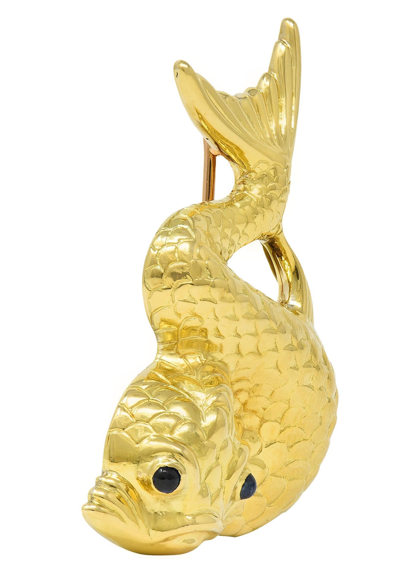 Designed a swirled koi fish with repoussé scaled body and fins 
Accented by 2.0 mm round sapphires - bezel set
Transparent medium blue in color
With high polish finish
Completed by hinged pinstem with locking closure
Stamped for 18 karat gold
Fully