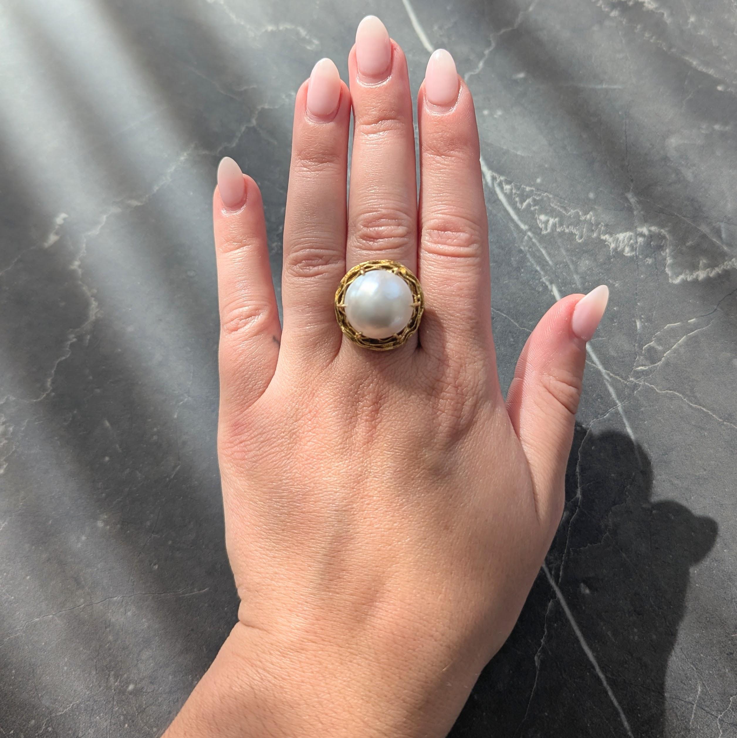 Centering a 17.0 mm round mabé pearl - white with strong iridescence
Prong set in a deeply grooved nest-like mounting
Flanked by tri-split shoulders
With grooved shank
Stamped for 18 karat gold
Fully signed for Tiffany & Co.
Circa: 1960s
Ring Size: