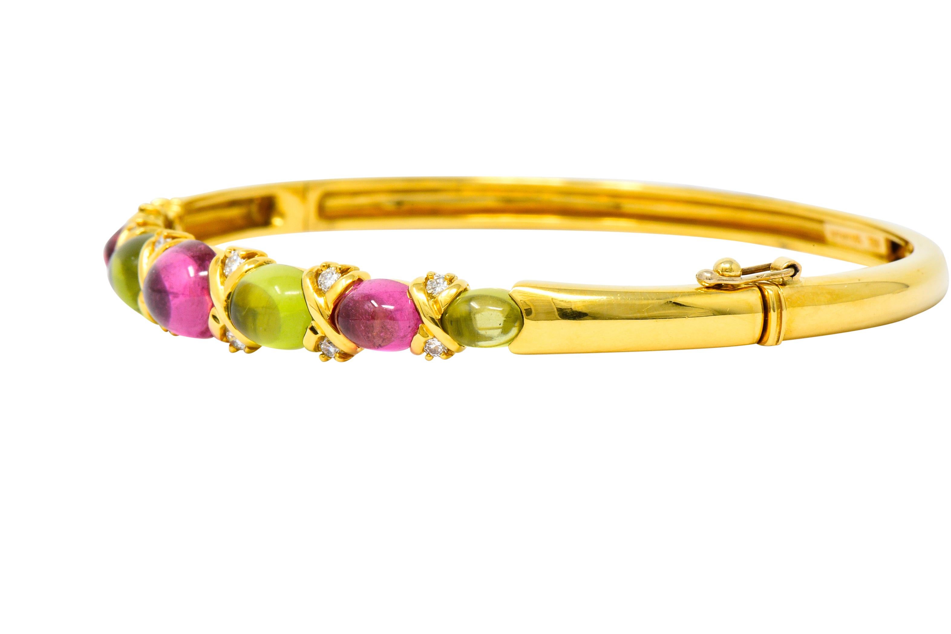 Hinged bangle bracelet set to front with oval cabochon peridot and pink tourmalines graduating in size from 4.0 x 5.0 mm to 7.0 x 8.0 mm

With polished X motif alternating between cabochons

Accented by round brilliant cut diamonds weighing