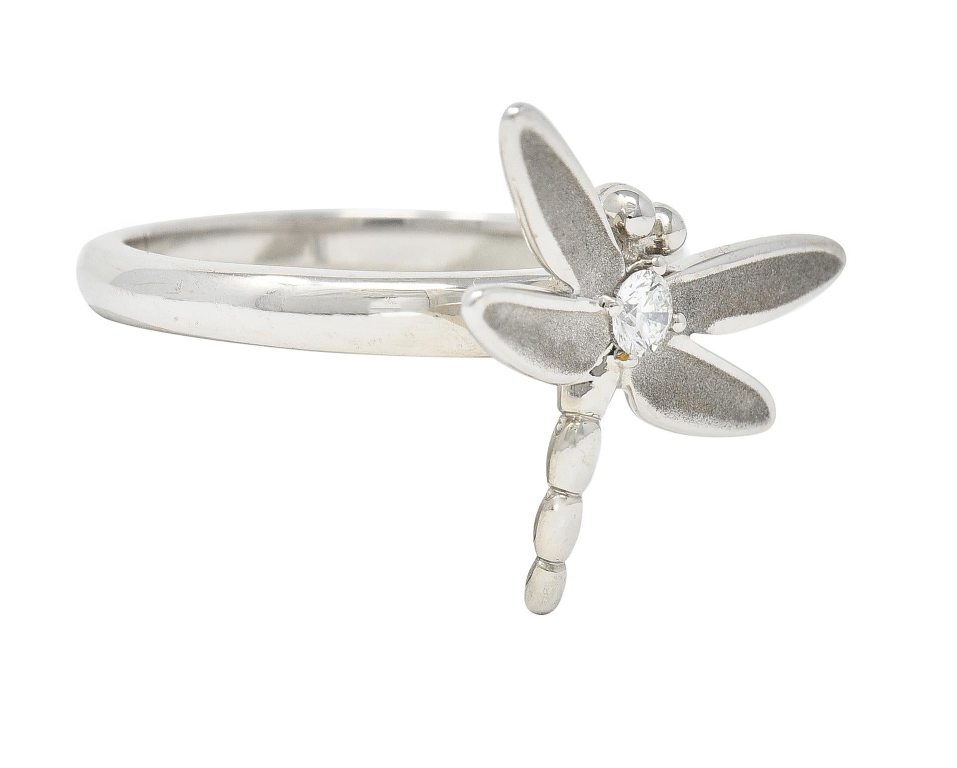 Designed as a stylized dragonfly with brushed matte wings, Centering a prong set round brilliant cut diamond. Weighing approximately 0.10 carat total. Eye clean and bright. With high polish finish. Stamped 750 for 18 karat gold. Fully signed for