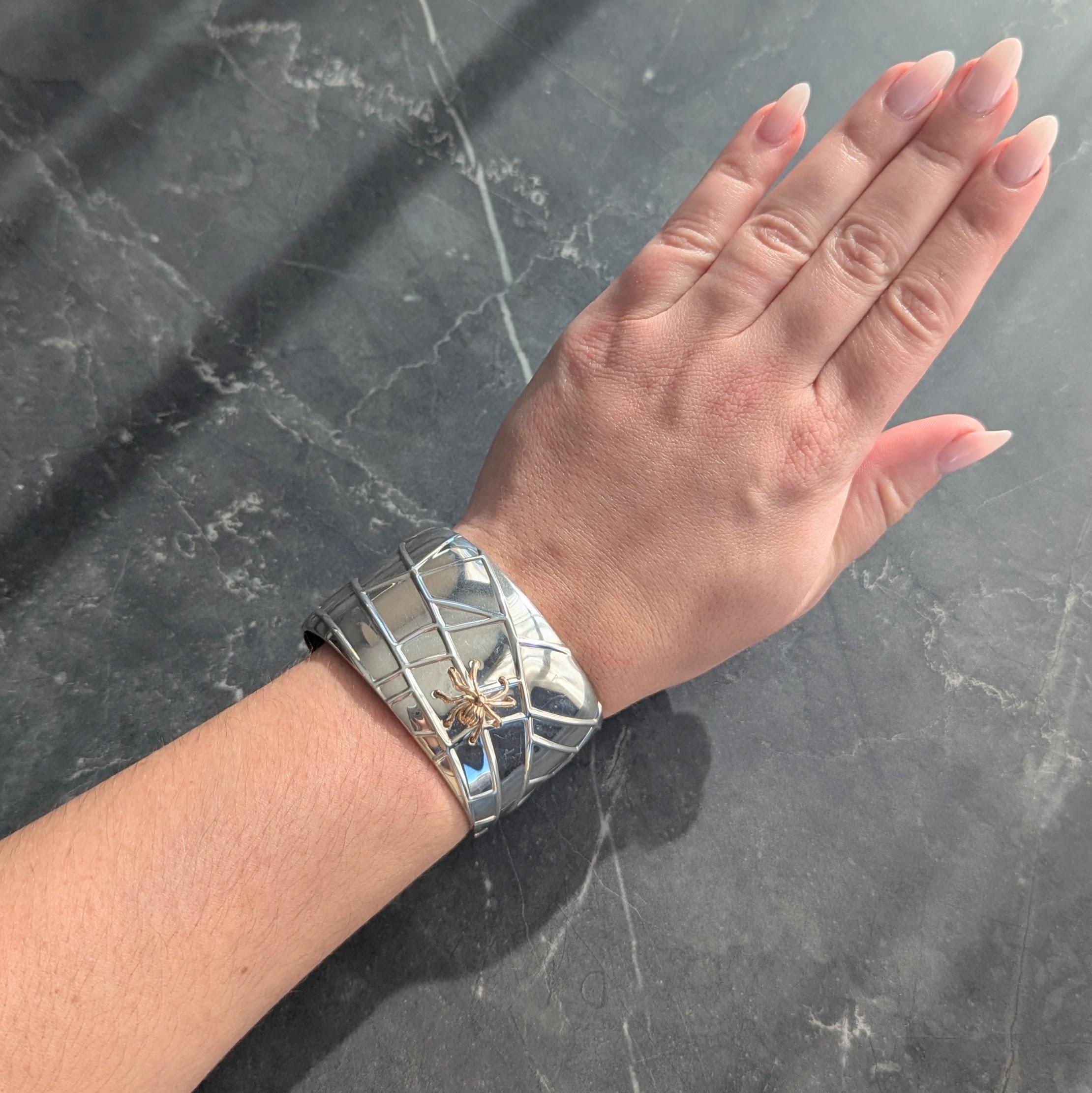 Bracciale largo in stile polsino in argento sterling.
Raffigurazione di una ragnatela con dettagli in rilievo
Applicazione di un ragno in oro giallo
Completato da terminali arrotondati
Con finitura lucida
Timbrato per oro 18 carati e argento