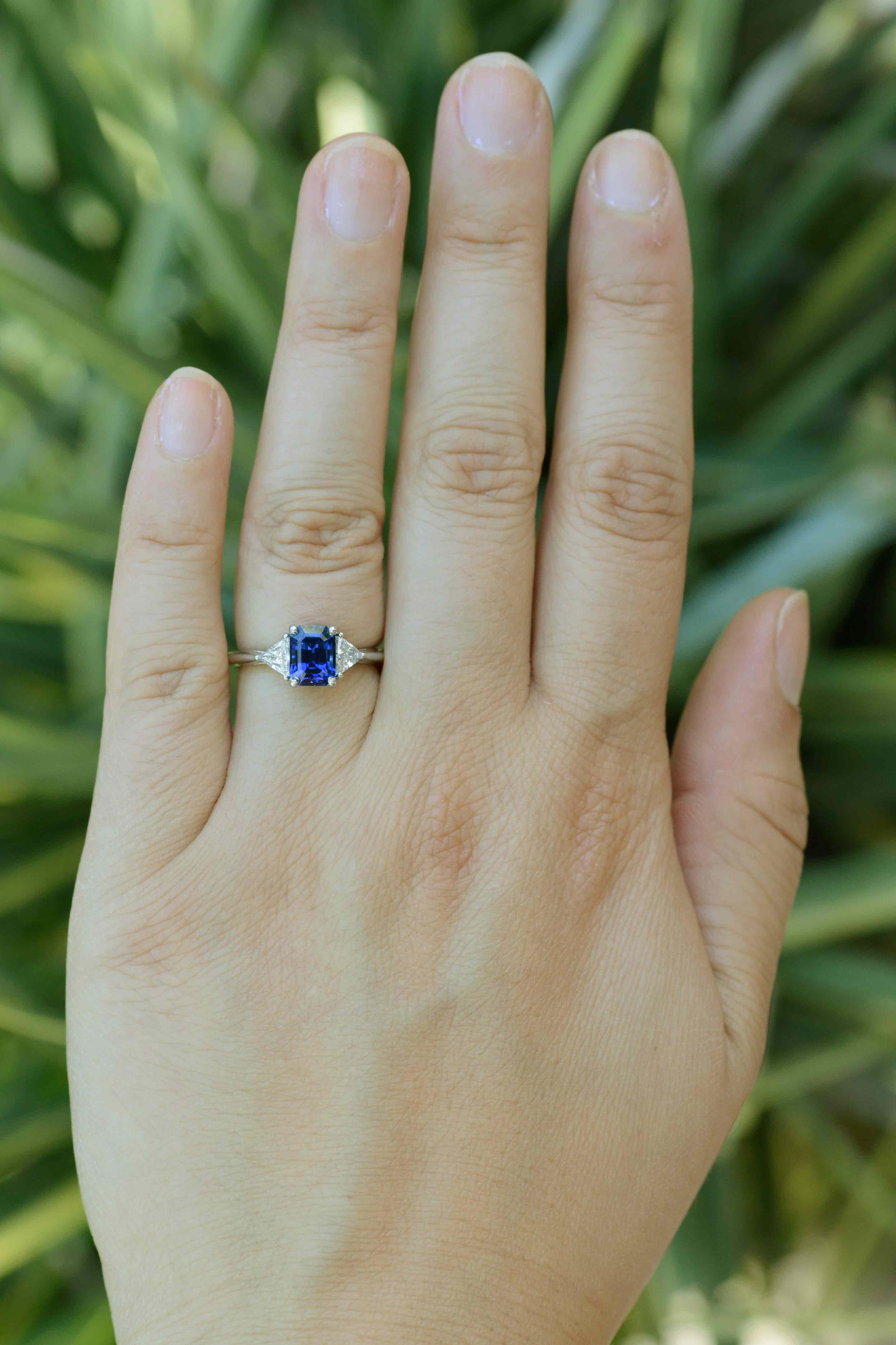 Signed Tiffany & Co. engagement ring. One luscious emerald cut sapphire weighting 2.13 carats takes the spotlight. Two triangular brilliant cut diamonds accent the bright blue gemstone. Examined and tested by the Tiffany Gemological Laboratory. Made