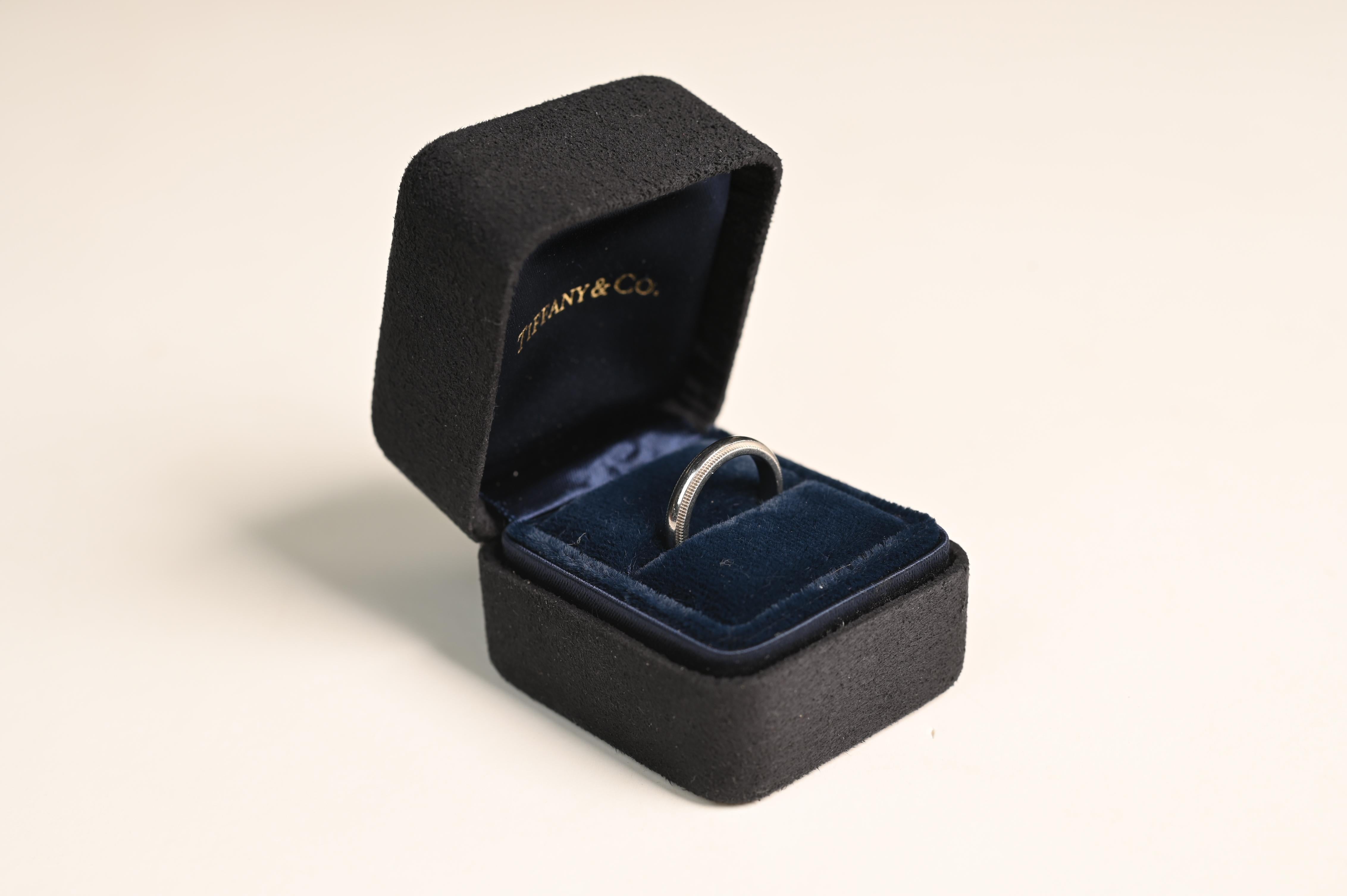 This exquisite Tiffany & Co. wedding band is a timeless symbol of love and commitment. Expertly handcrafted in platinum, the band features a delicate milgrain edge, adding a touch of vintage-inspired elegance to its classic design. The polished